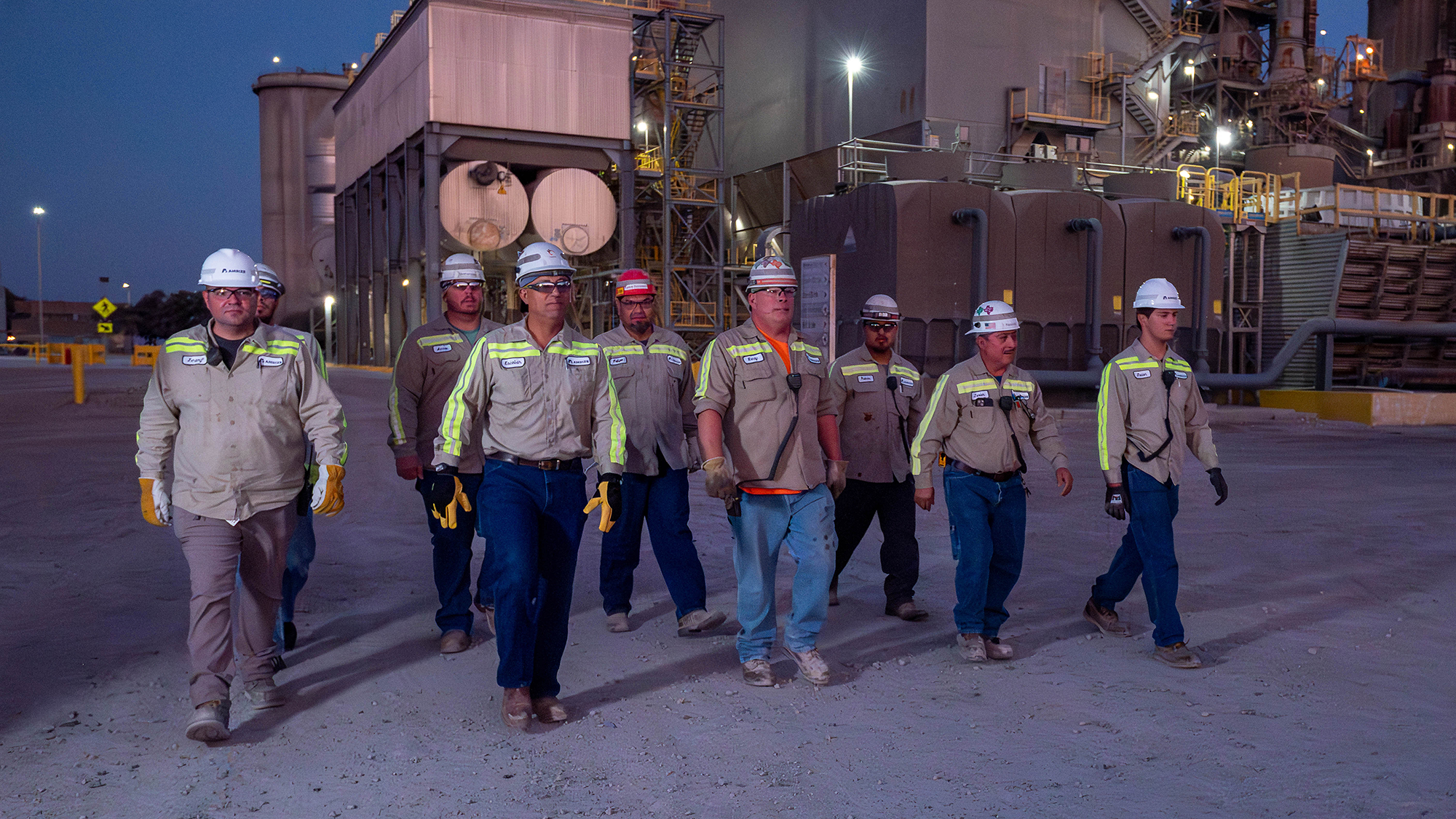 A group of employees at an operational site walk towards the camera with a factory behind.