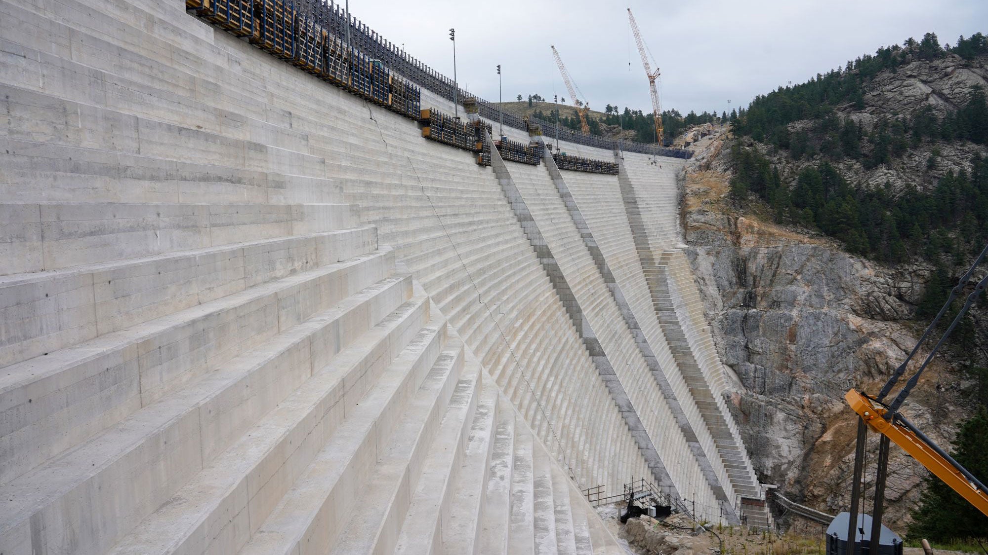 Massive stepped concrete spillway under construction at Gross Reservoir Dam, illustrating the 131-foot expansion project.