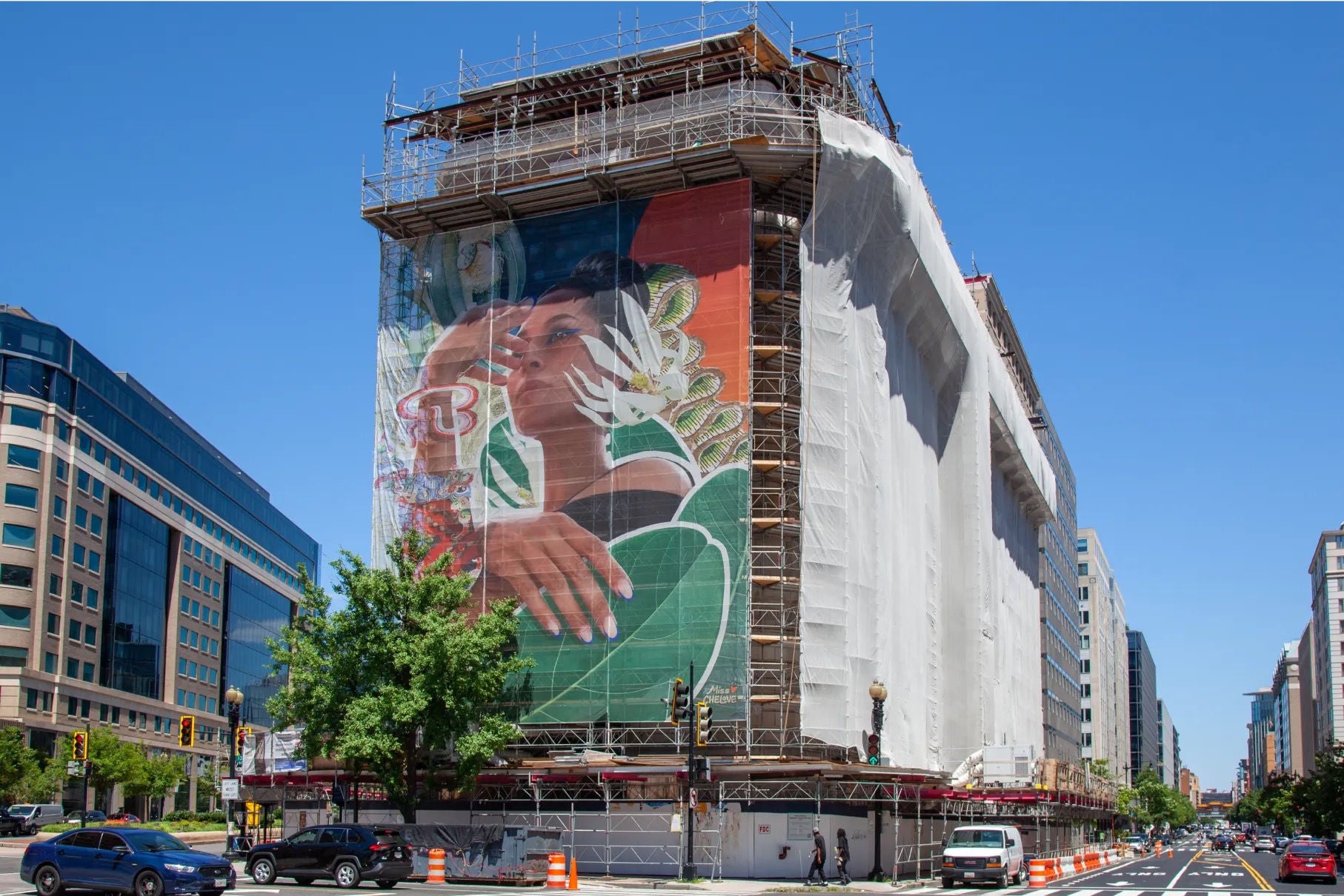 Un bâtiment couvert d’échafaudages sur trois côtés, le quatrième côté présentant une grande peinture murale.
