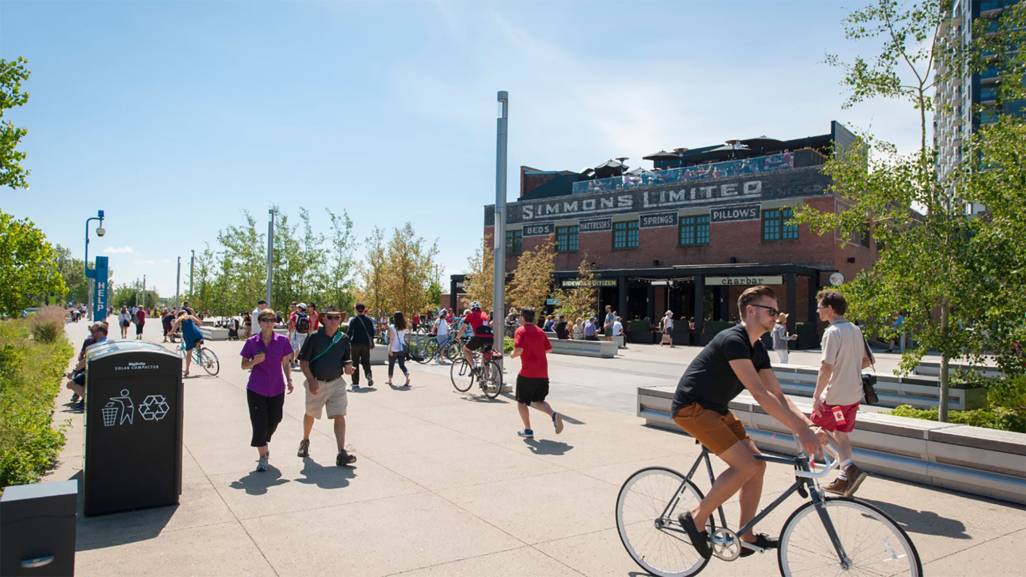 Pedestrians and cyclists on Calgary’s RiverWalk passing the historic brick Simmons Building in East Village.