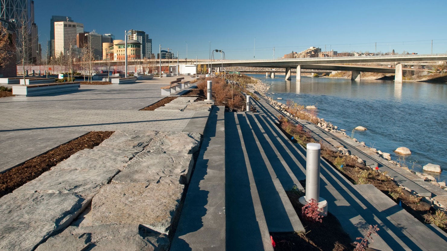 Modern riverside plaza in East Village Calgary with tiered concrete steps and views of the downtown skyline.