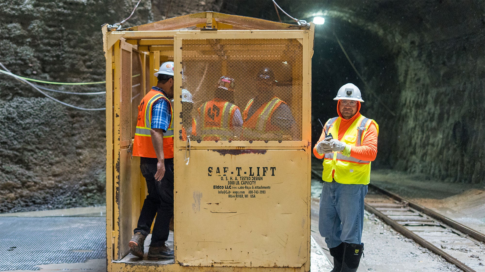 Construction workers standing inside and next to a yellow personnel cage during underground construction at the Mill Creek Tunnel project in Dallas, Texas.