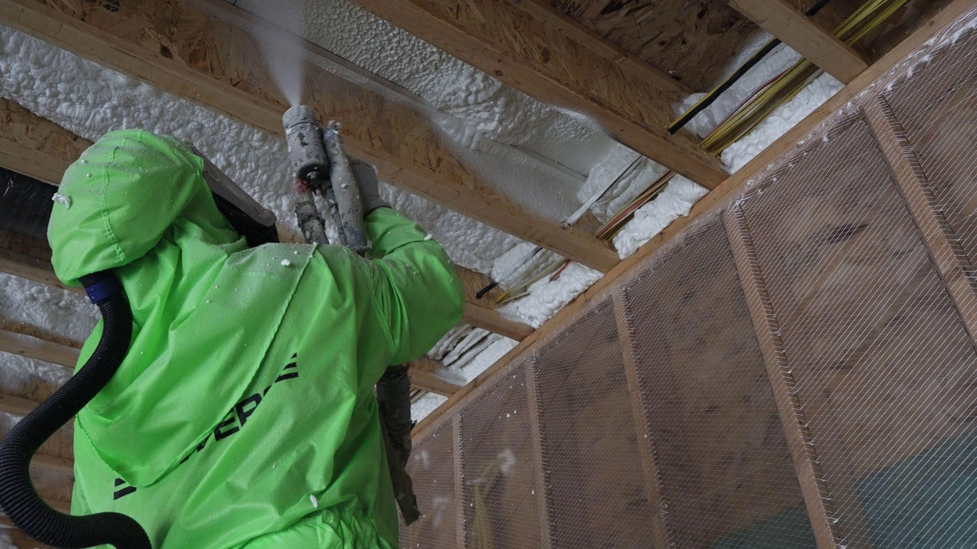 A contractor applies Enverge EasySeal .5 open-cell spray foam insulation to roof deck framing, expanding to fill cavities and seal air gaps.