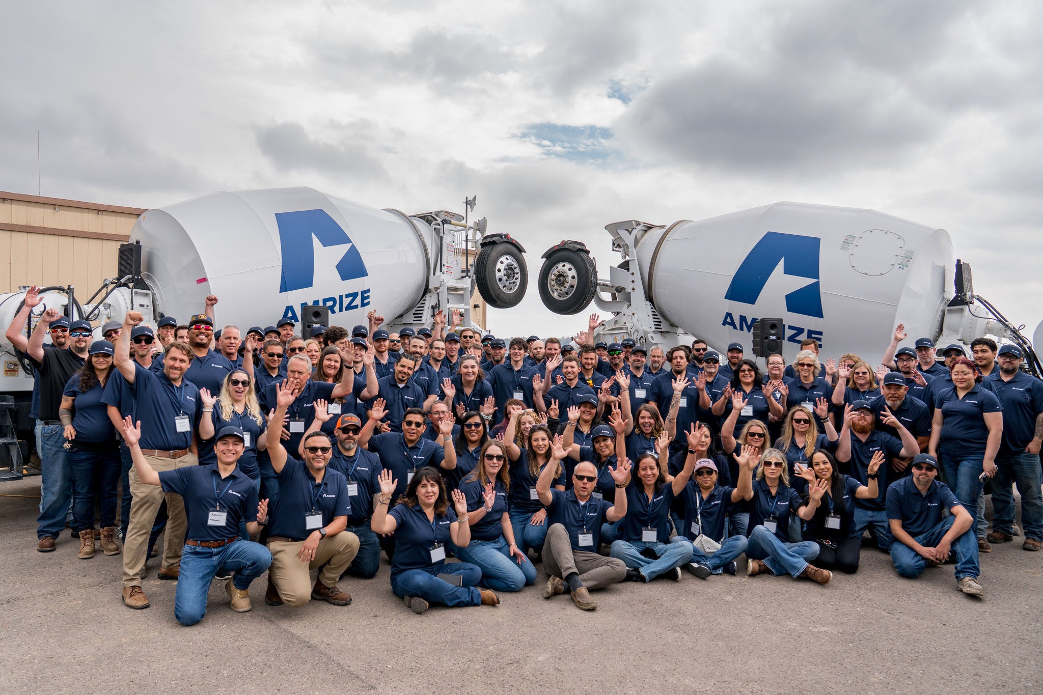 A group of employees wave and cheer in front of two trucks