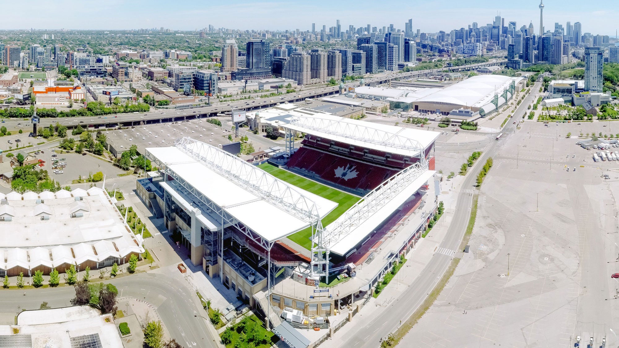 Aerial view of BMO Field stadium in Toronto, Ontario, featuring the green pitch, white roof structures, and the Toronto city skyline with the CN Tower in the background.