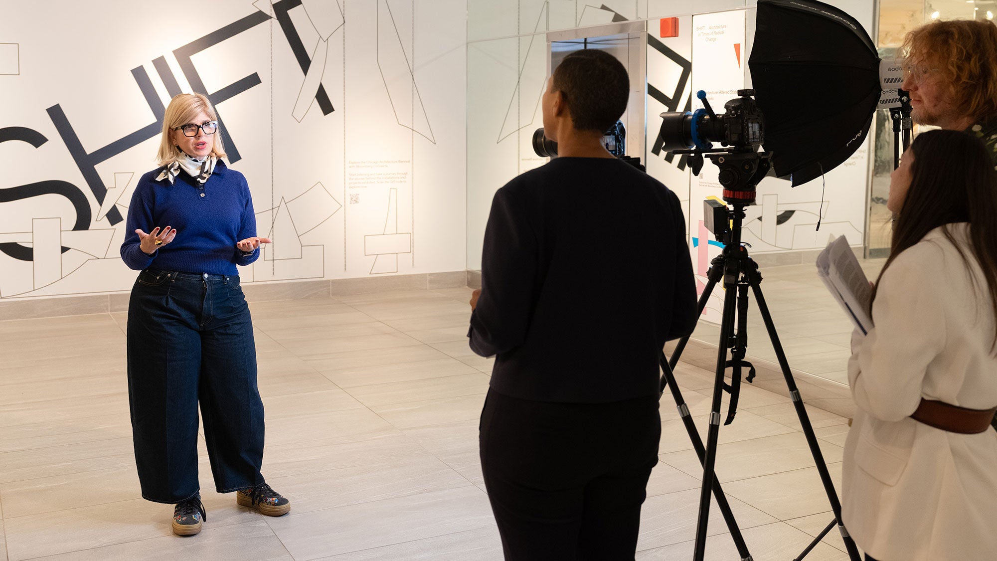 A woman is interviewed by a film crew standing in front of a wall with the word “Shift” on it.