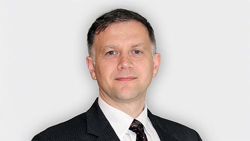 Headshot of Vassil Draganov wearing a pinstripe suit, white shirt, and patterned tie.
