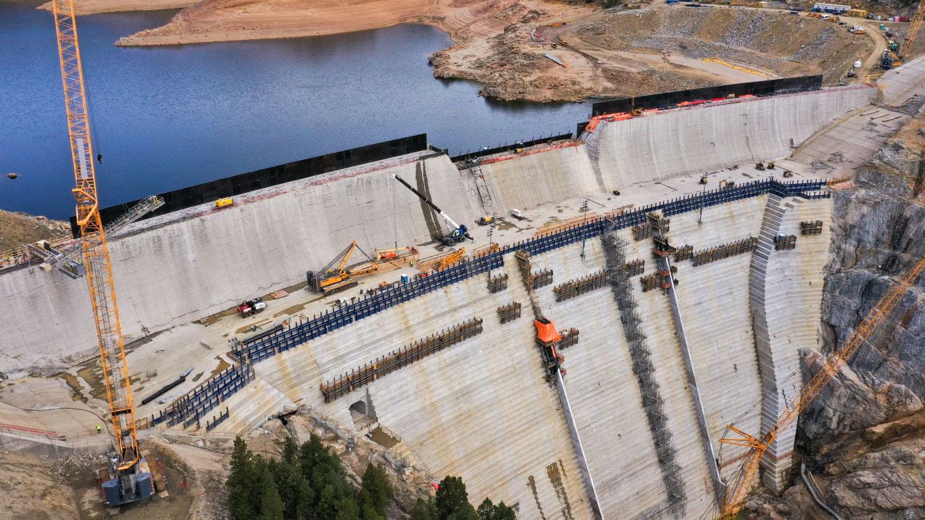 A large concrete dam being constructed in front of a clear blue lake