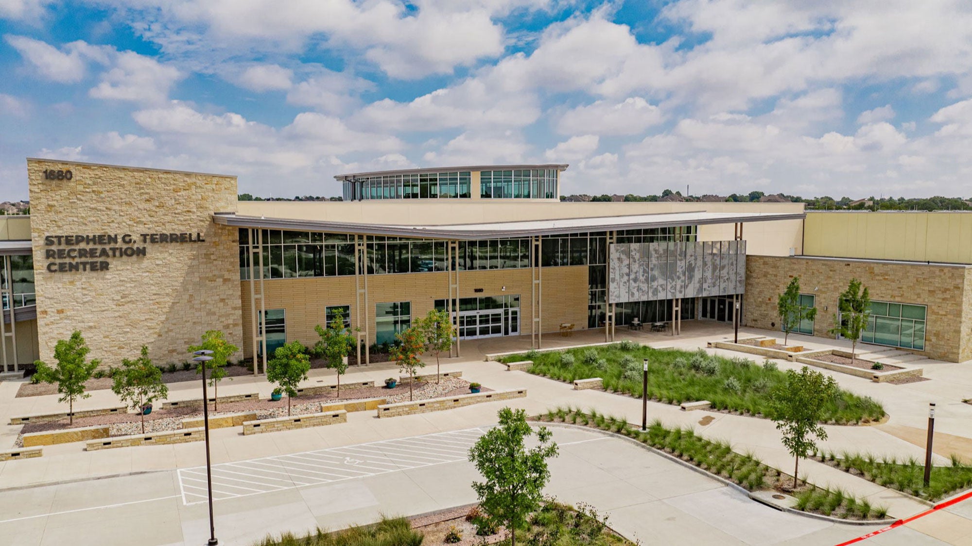  Entrance to the Stephen G. Terrell Recreation Center under a bright blue sky with surrounding green trees and yellow hardscape with Amrize concrete.