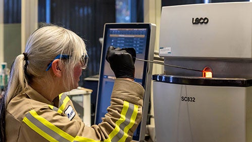 A woman checks a monitor next to a machine in a plant