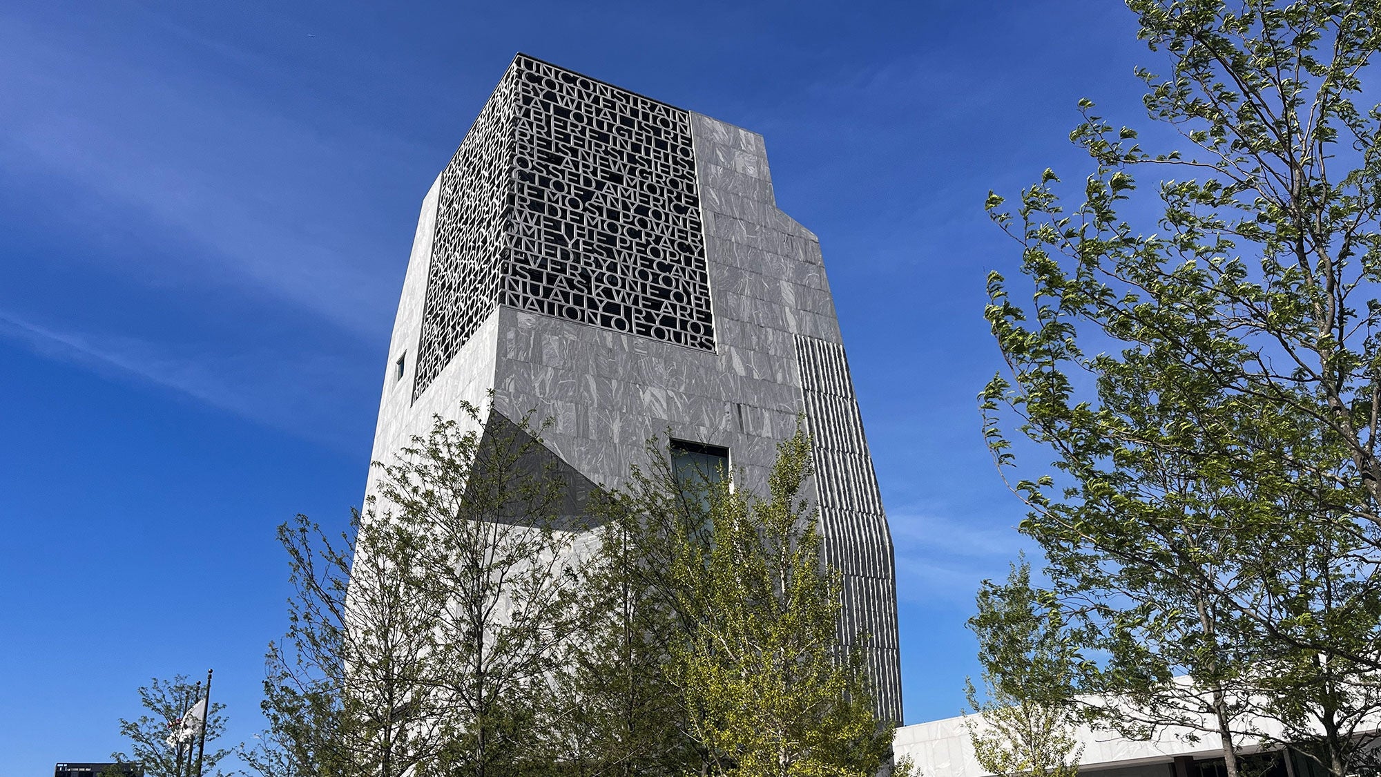 Low-angle shot of the tower at the Obama Presidential Center in Chicago, featuring a concrete letter facade under a bright blue sky.