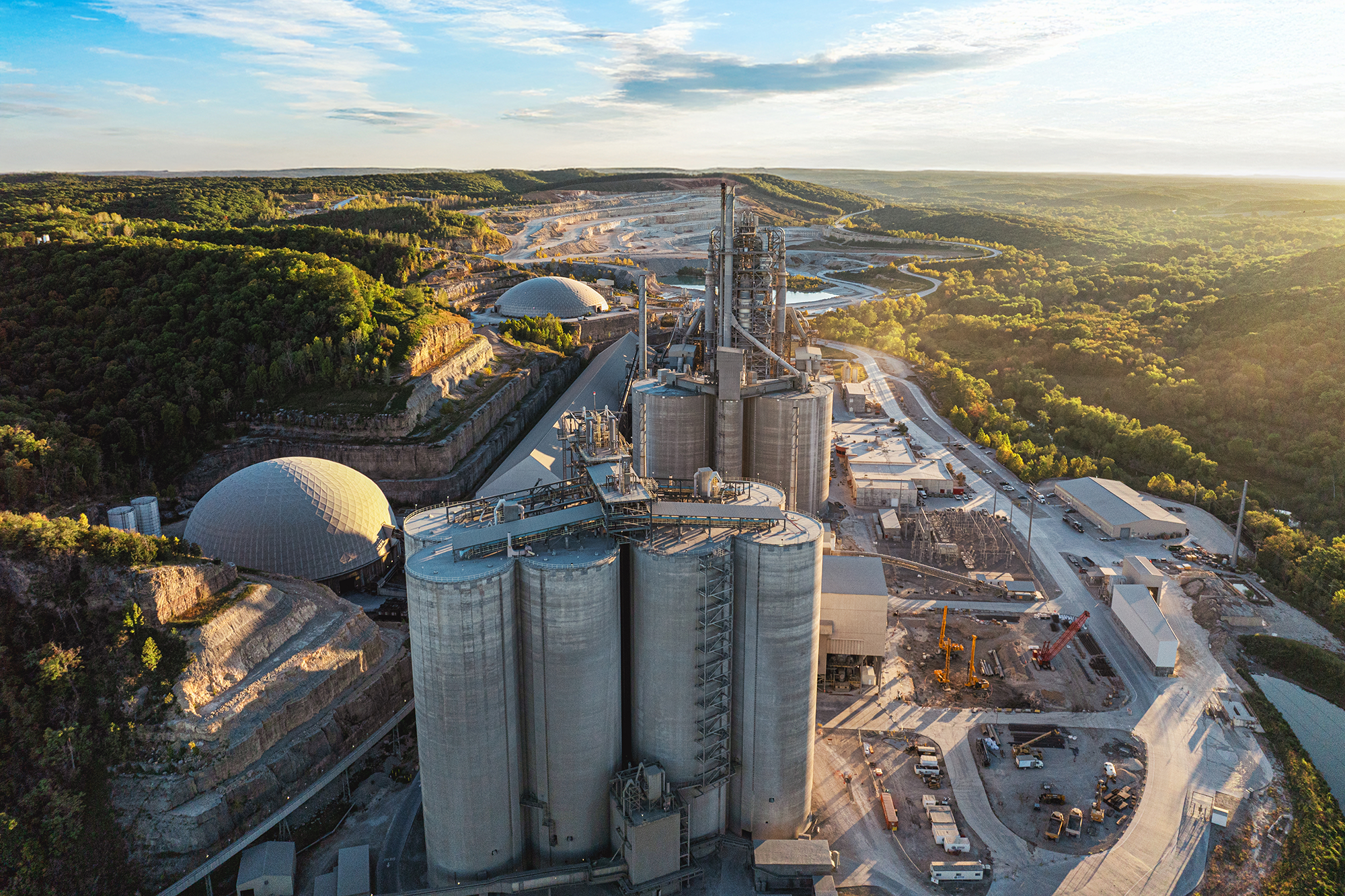 A large cement plant set among rolling green hills