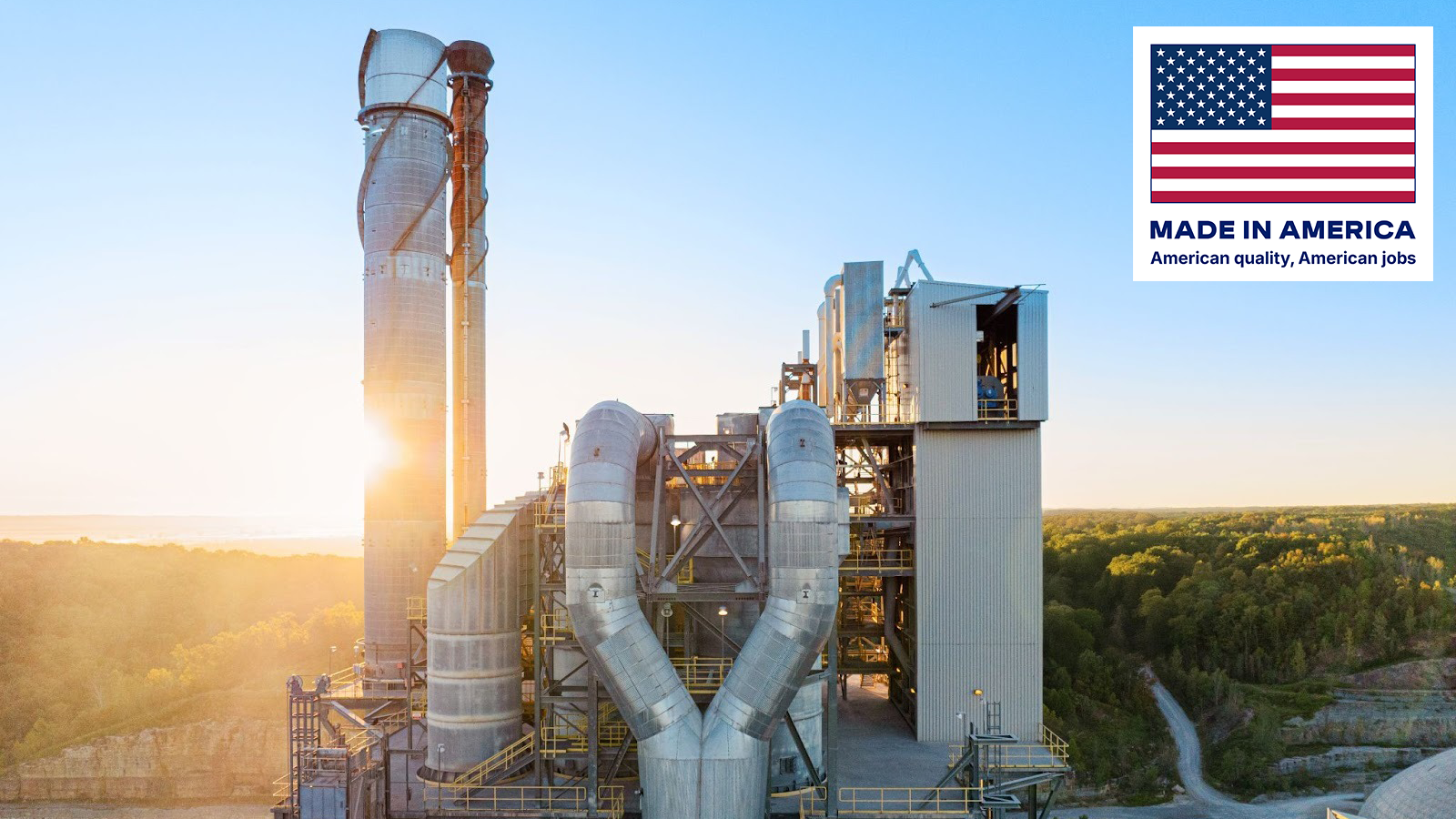 The sun rising behind the stack of a cement plant surrounded by green hills