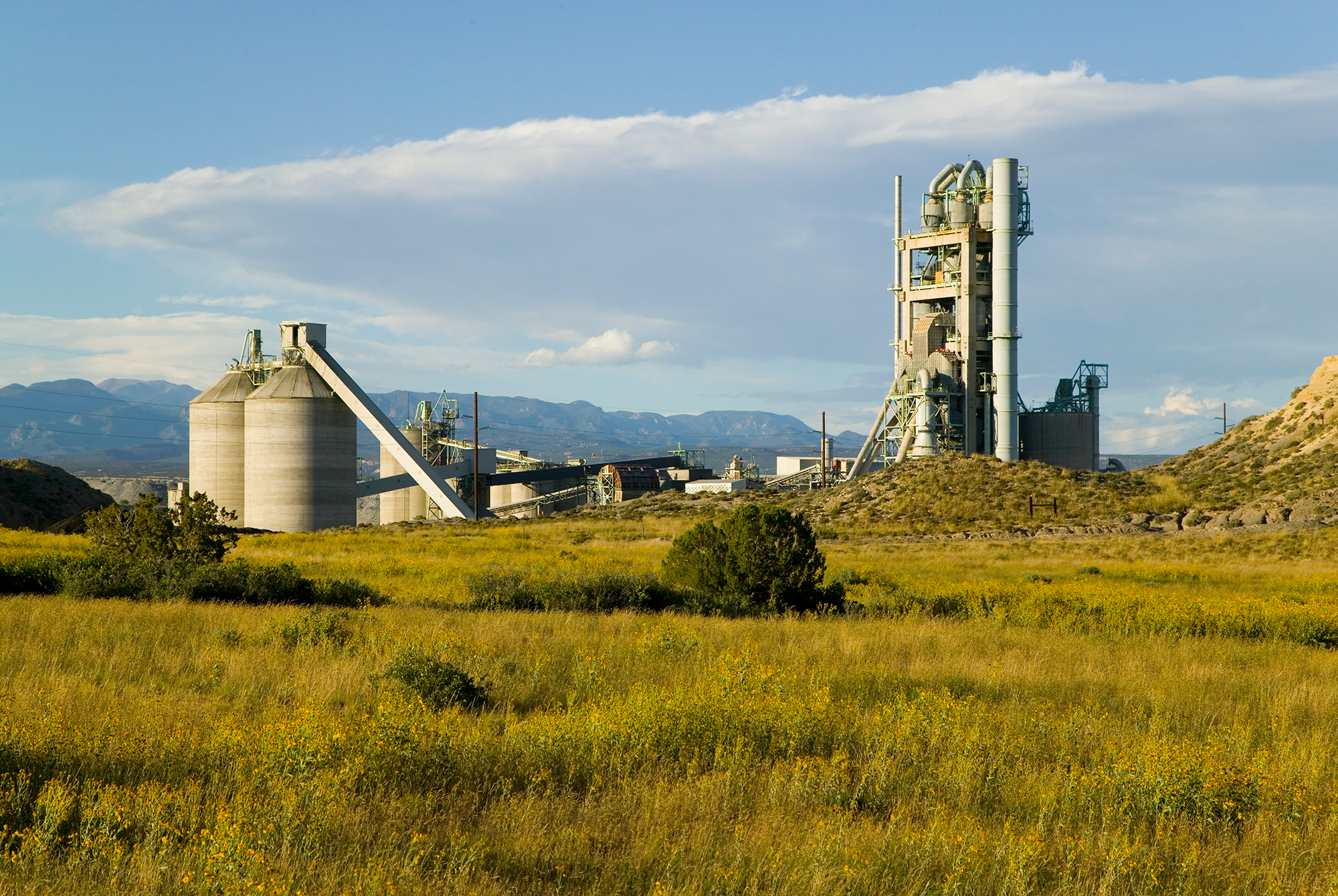 A cement plant in the middle of a green field with mountains in the background