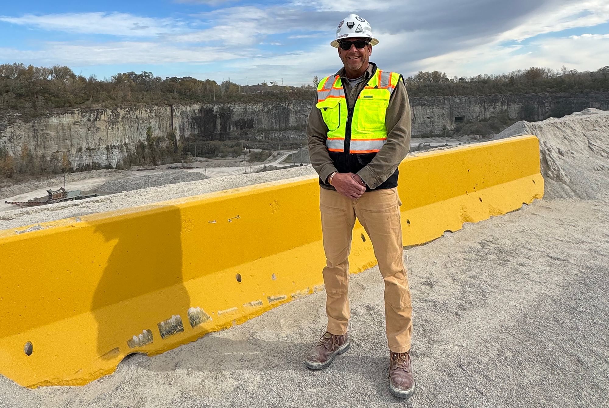 A man in a hard hat stands in front of a quarry
