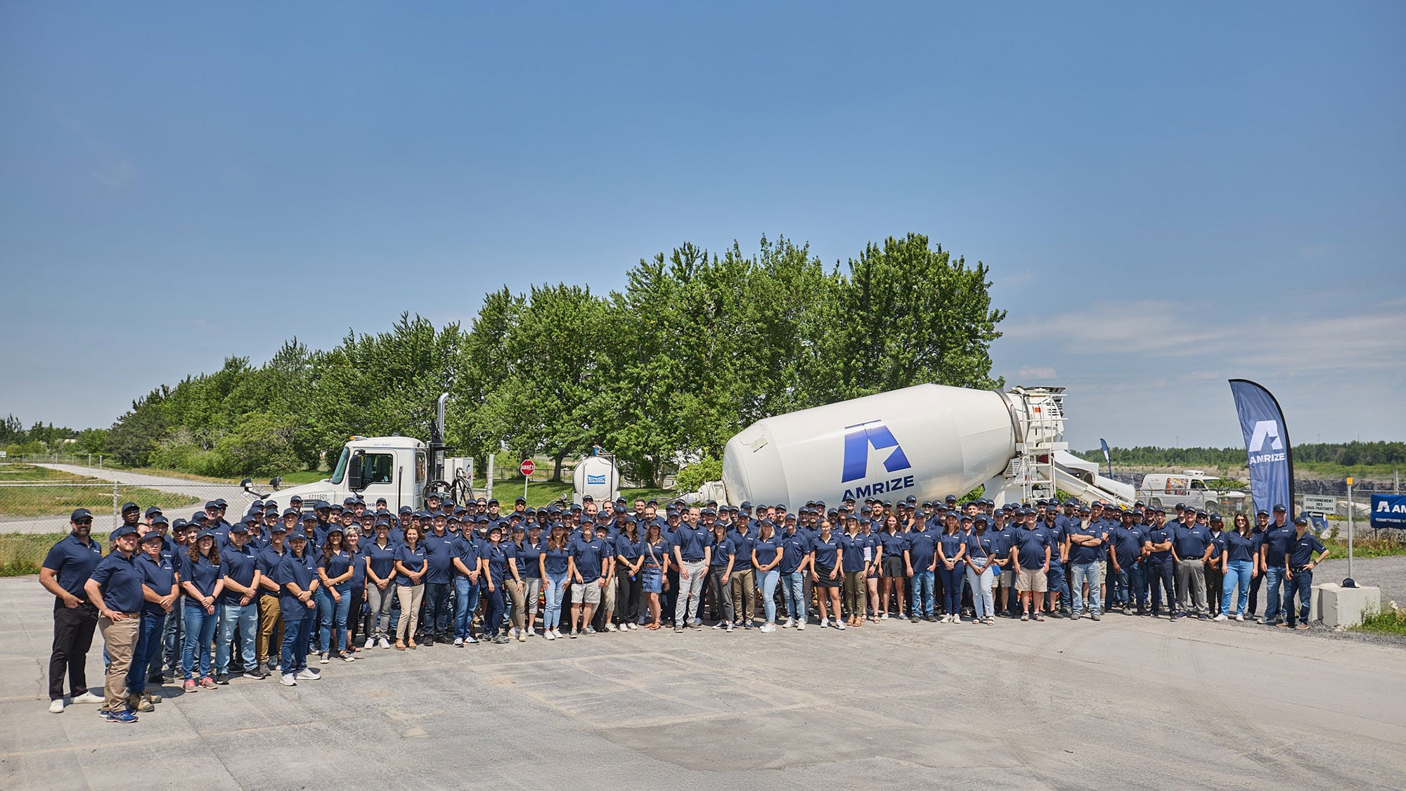 Un grand groupe d’employés portant des chandails bleu marine devant un camion-malaxeur avec des arbres à l’arrière-plan.