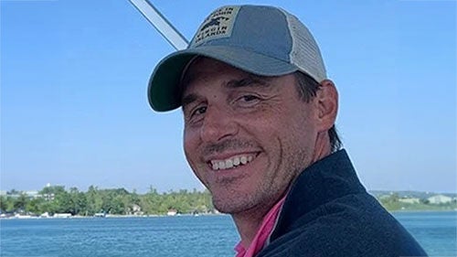Michael Finnegan wearing a baseball cap and dark pullover smiling on a boat outdoors.