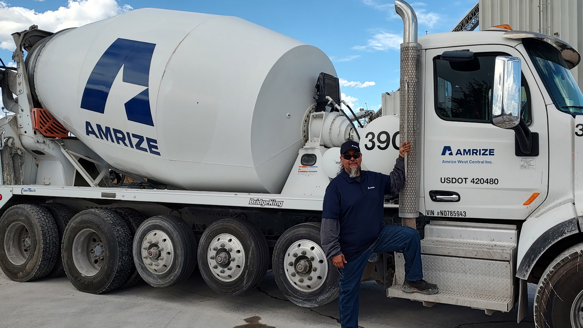 A ready-mix driver stands next to his truck on a beautiful day