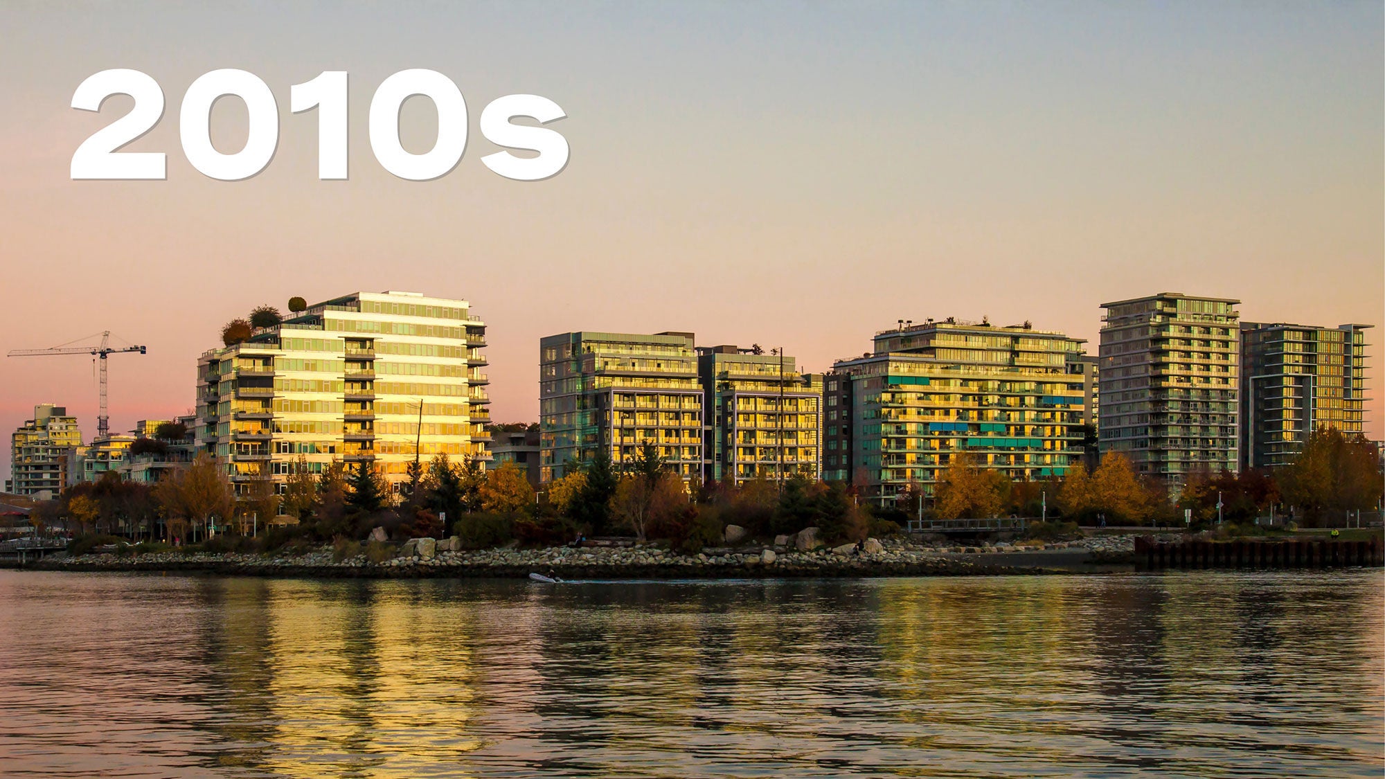 Vue du coucher du soleil sur un paysage urbain avec des gratte-ciels modernes reflétant une lumière chaude sur une rivière calme. Le ciel est un doux dégradé de rose à bleu. L’inscription « années 2010 » est en caractères gras blancs au-dessus. 