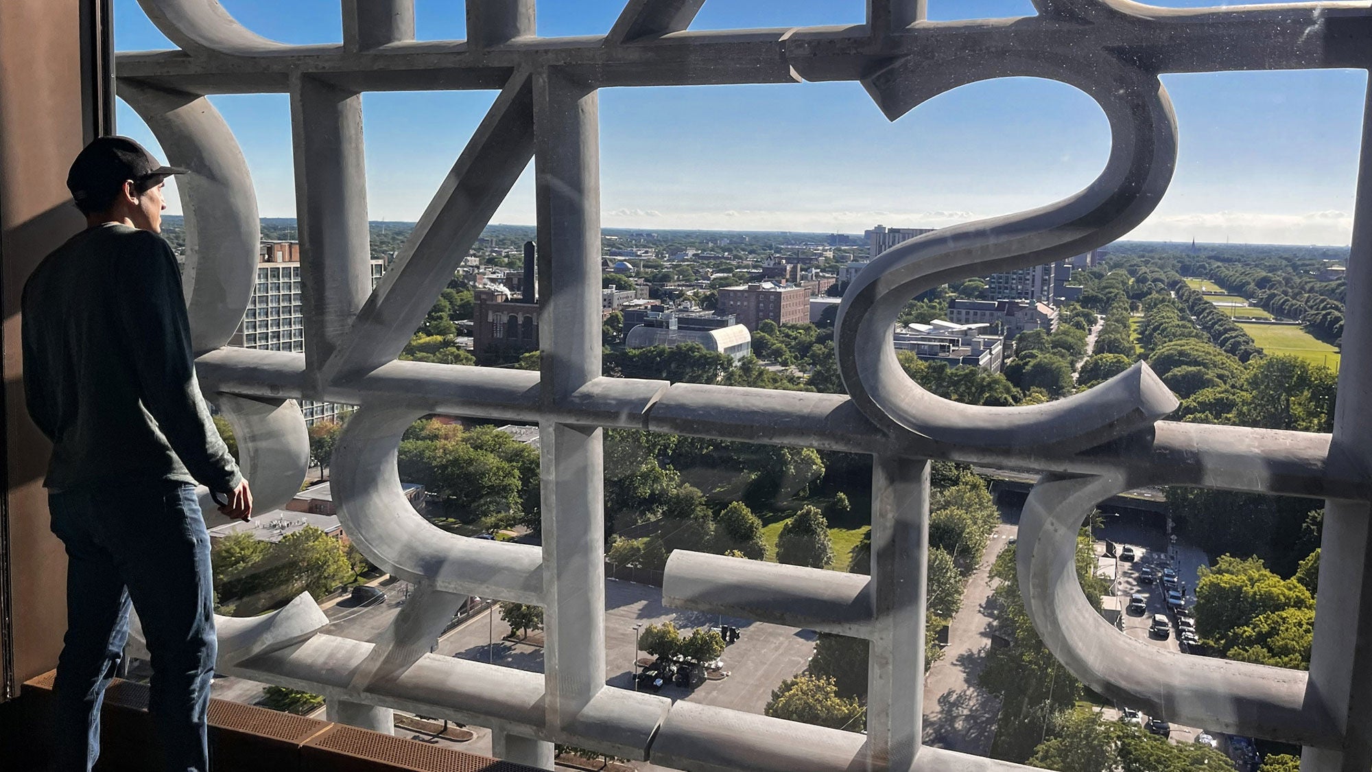 A man looking out of a high-rise window through the installed concrete letter facade of the Obama Presidential Center tower in Chicago.