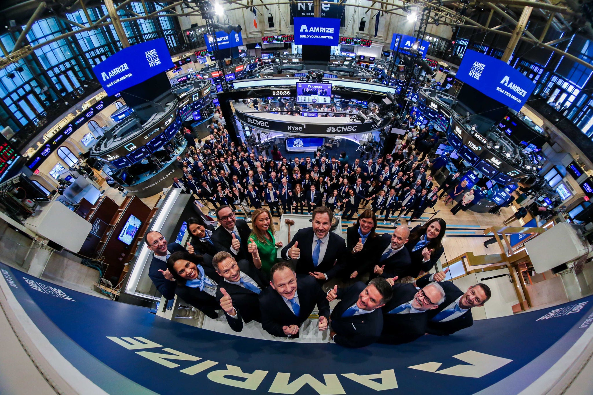 A group of executives stand on a podium above the New York Stock Exchange trading floor