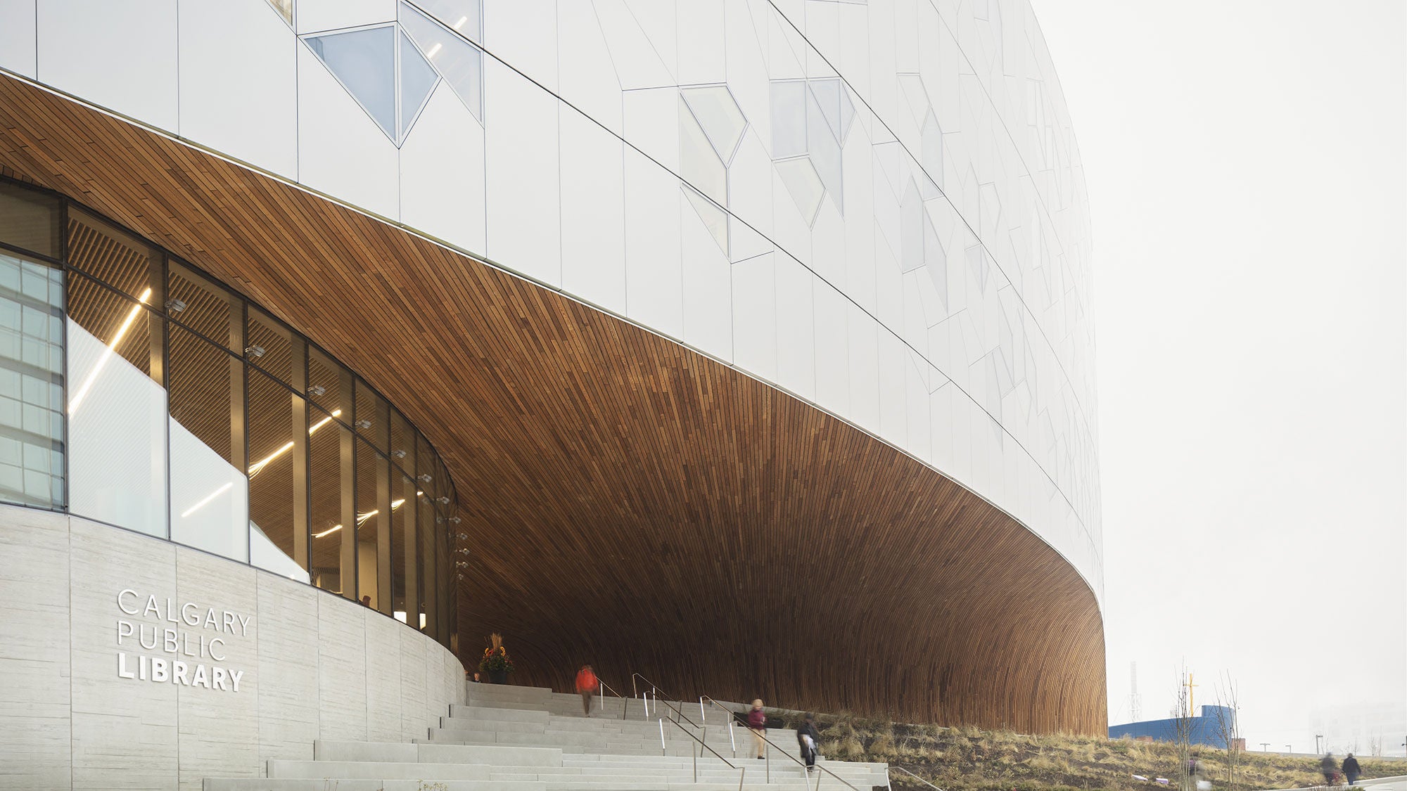 Modern architectural entrance of the Calgary Central Library with a large underbelly and concrete stairs.