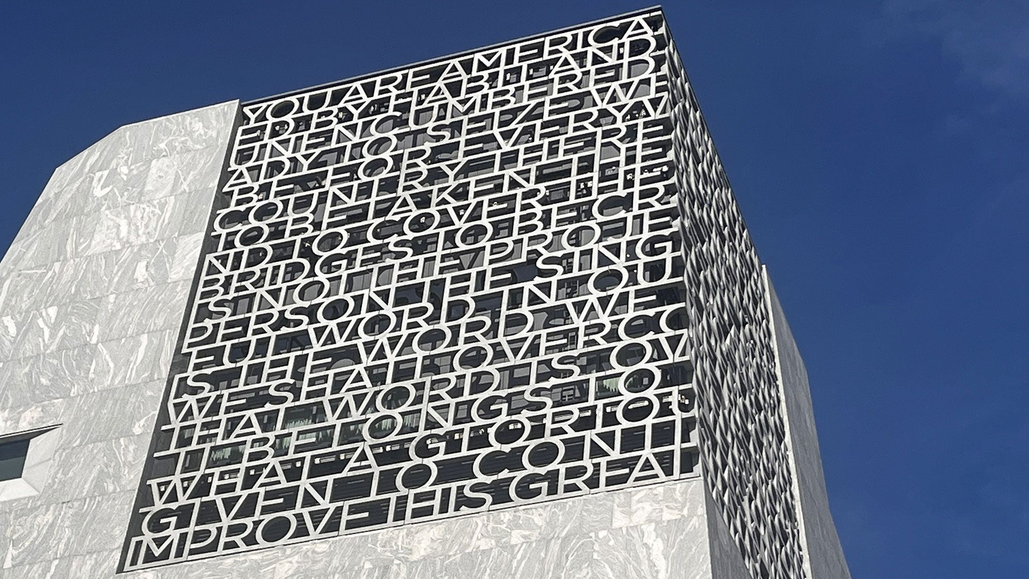 Exterior view looking up at the Obama Presidential Center tower featuring President Obama's Selma speech quote carved into the custom concrete facade against a clear blue sky.