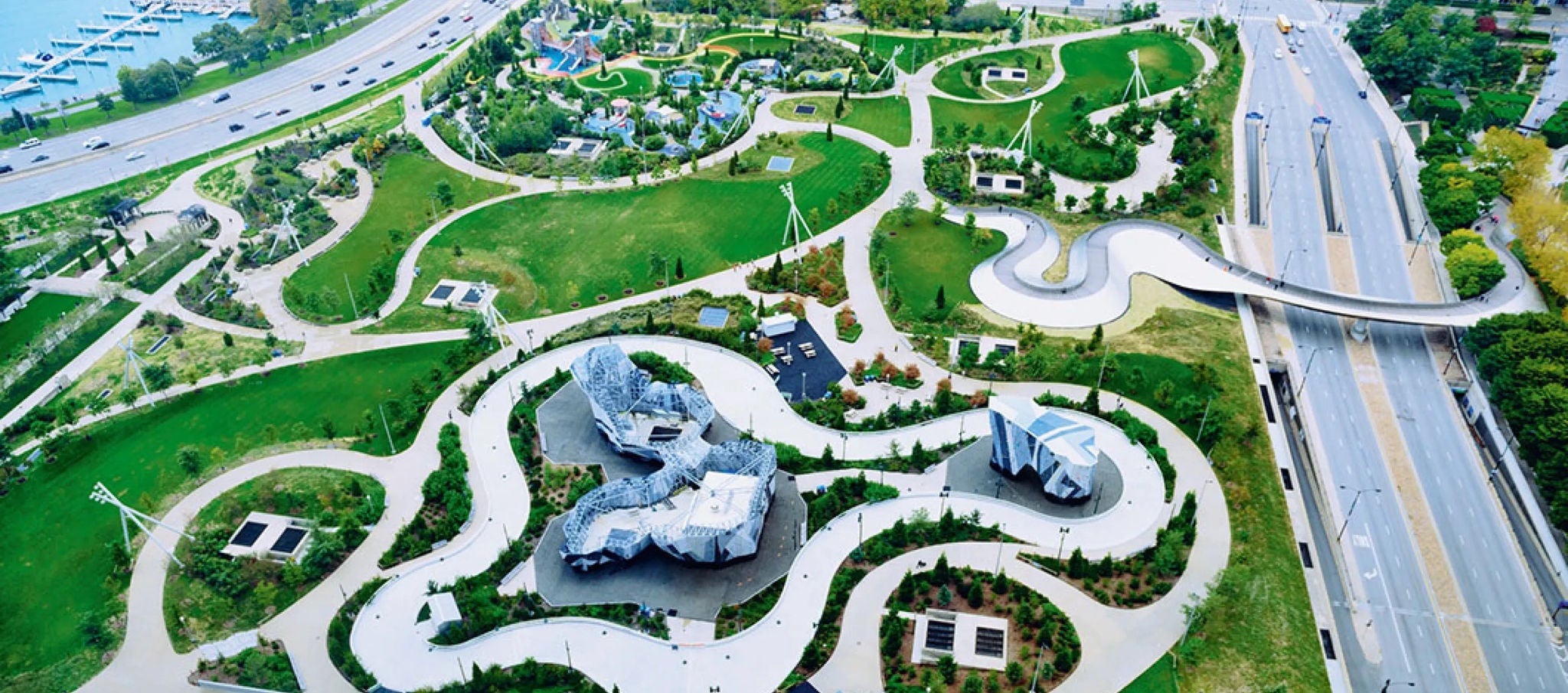 Aerial view of Maggie Daley Park in Chicago with winding pathways, green spaces, and pedestrian bridge in the distance