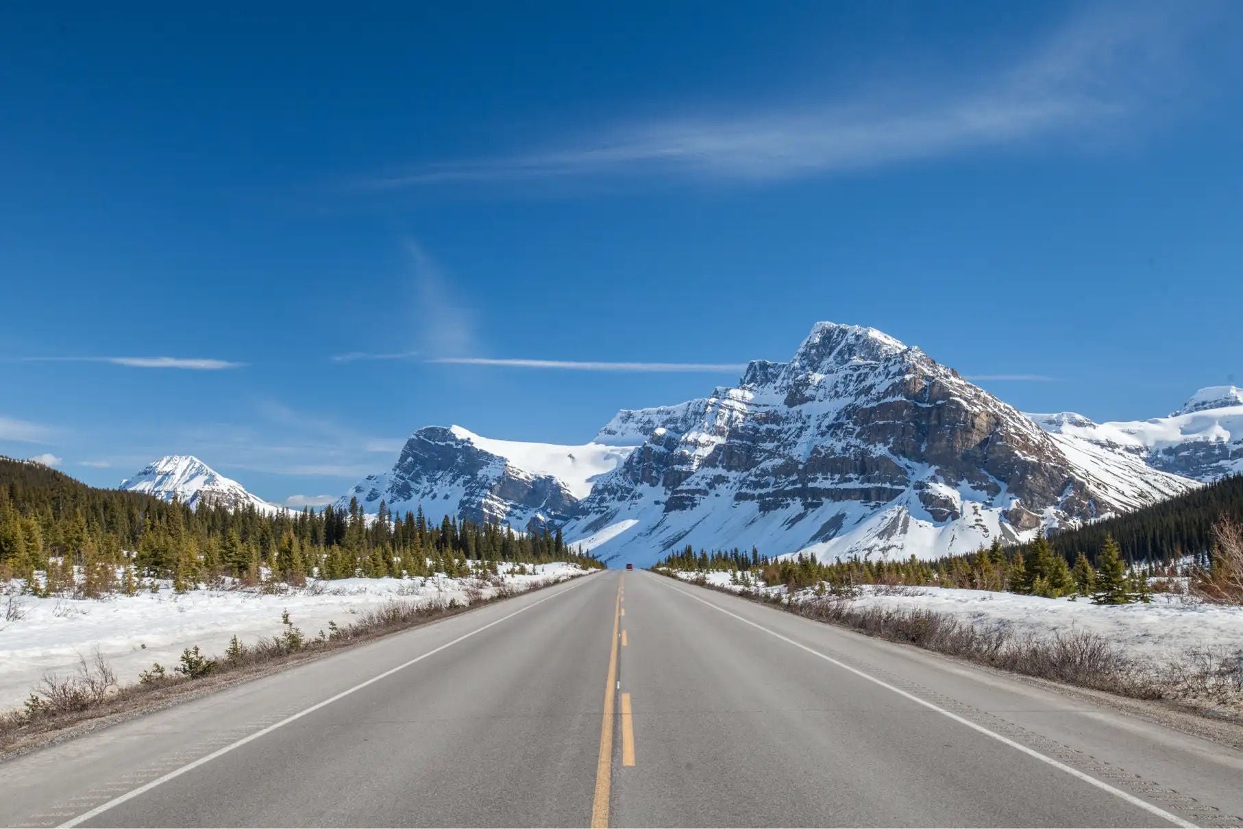 A two-lane road running through a mountainous, snow-covered environment.