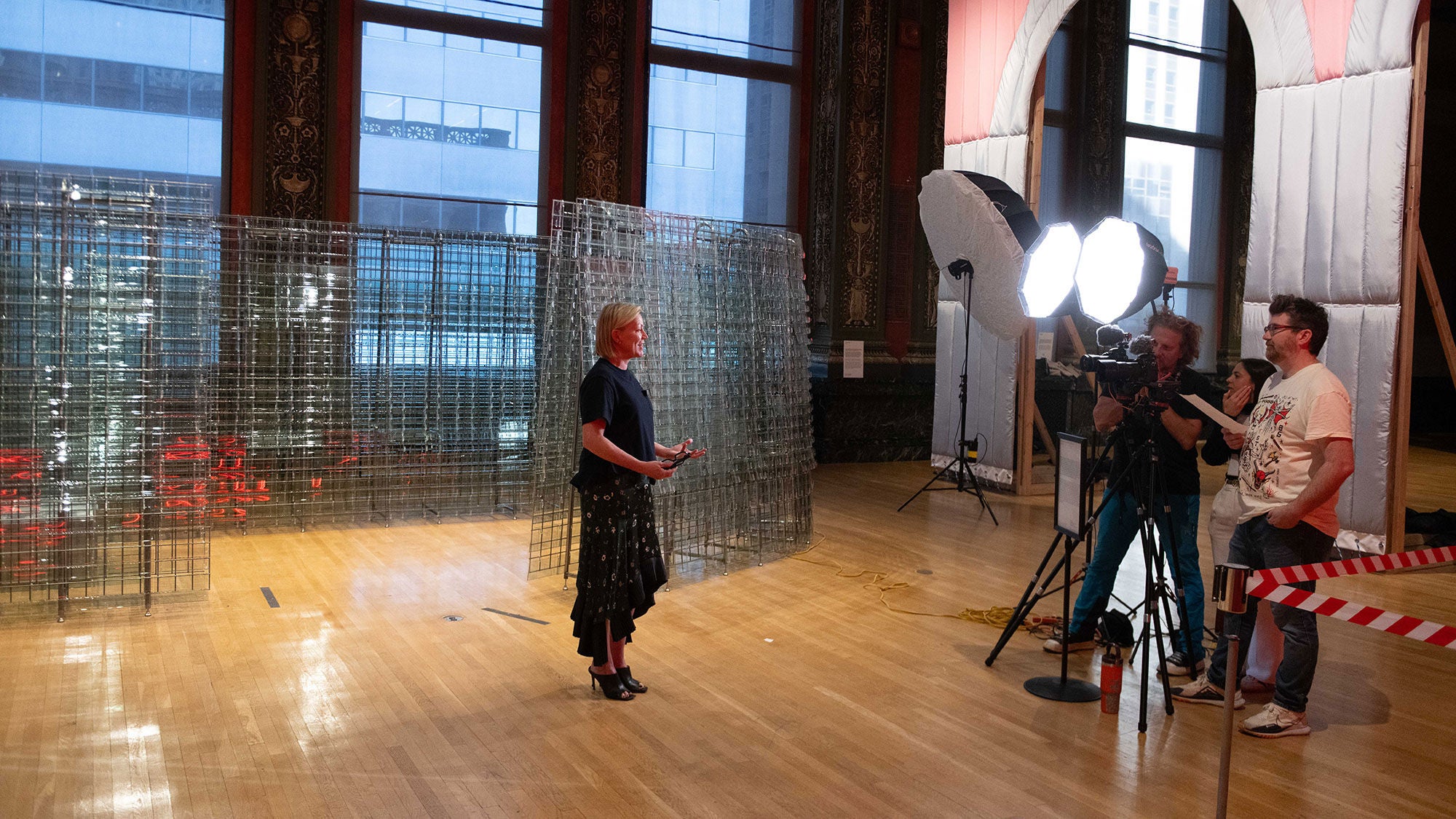 Standing in front of an art installation, a woman is interviewed by a film crew.