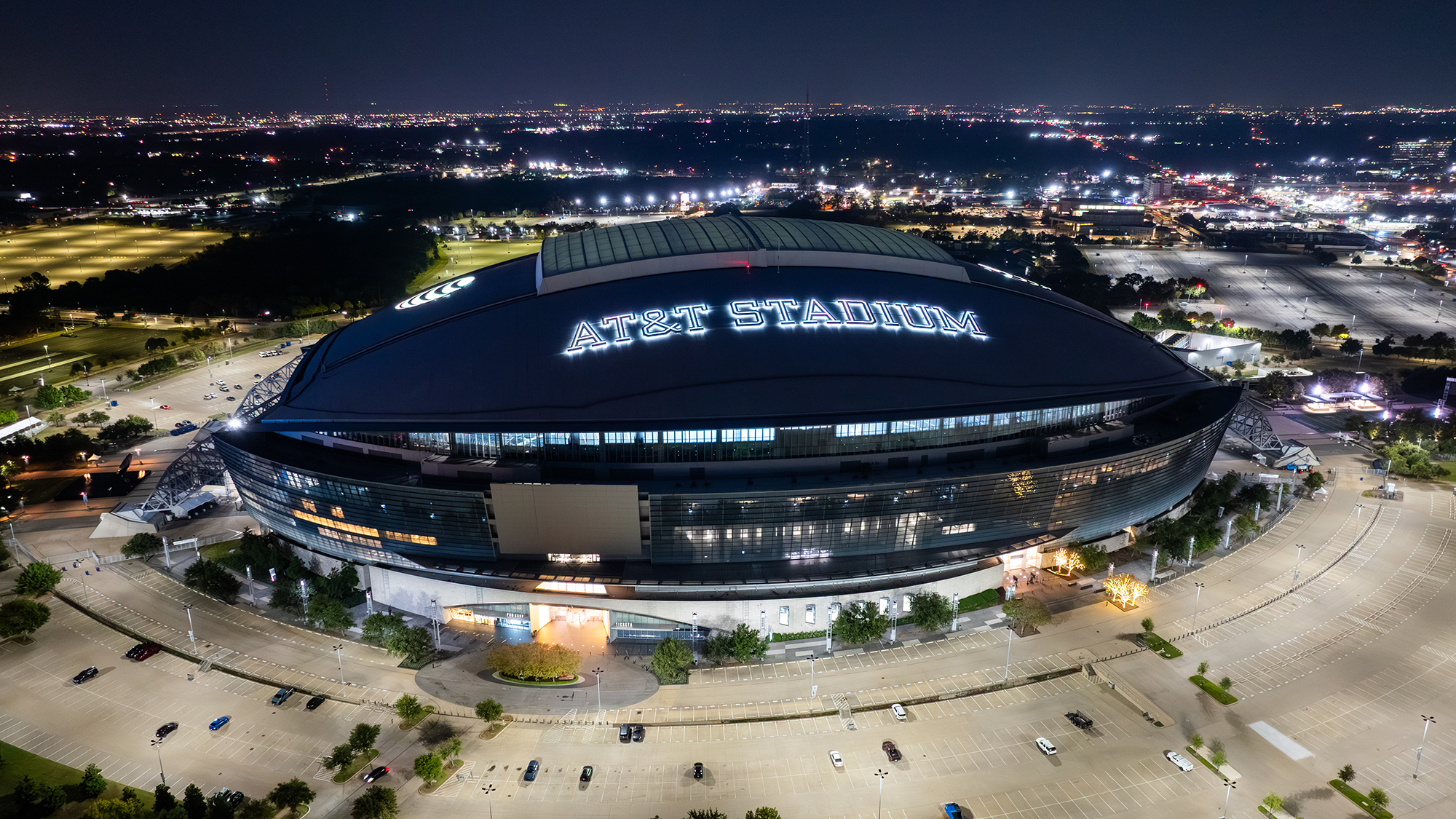 An aerial image of a stadium by night with the name lit up on the large, retractable roof