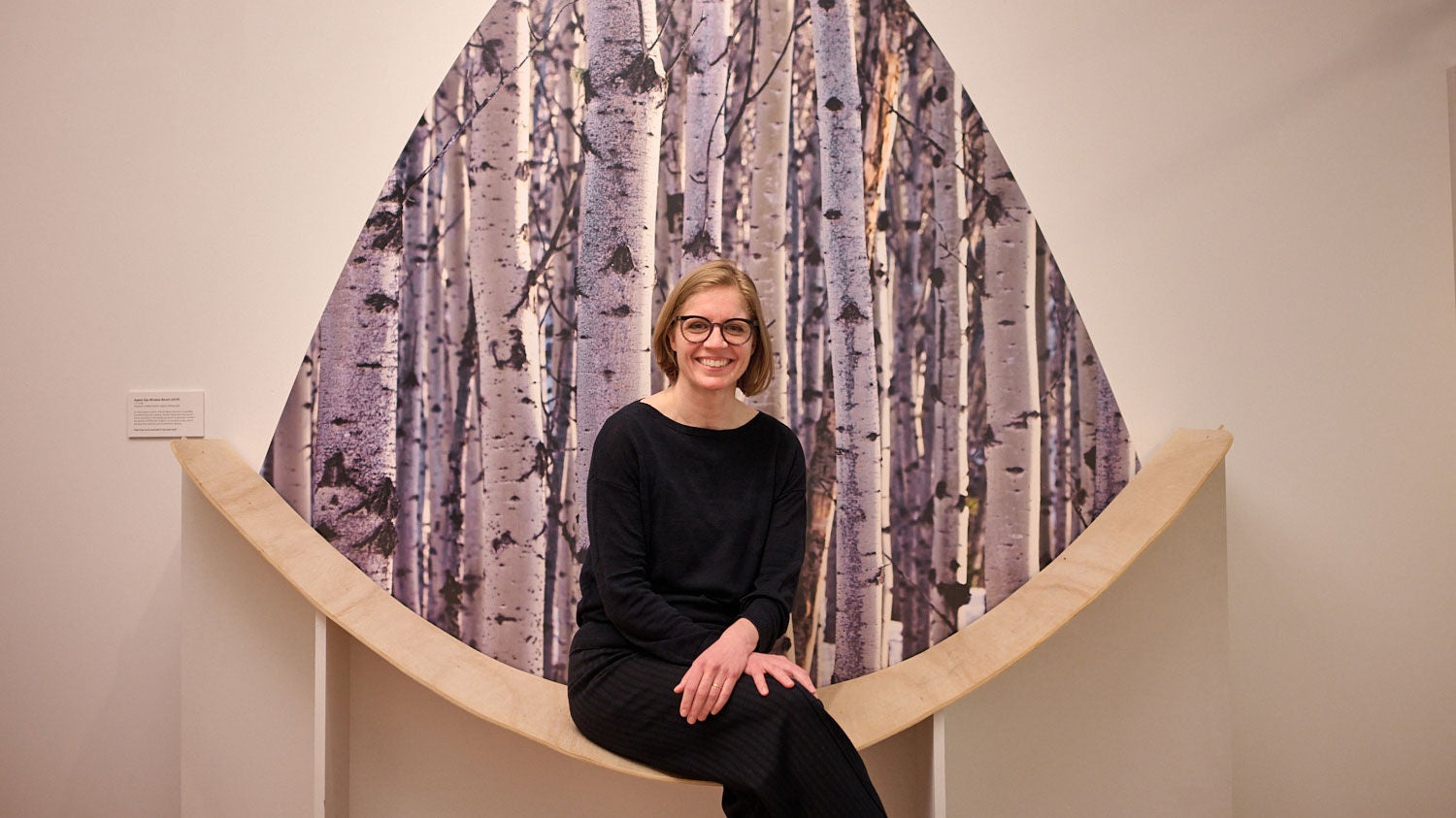 Architect Juliane Wolf sits in a full-scale, eye-shaped bench mockup at Studio Gang’s Chicago Architecture Biennial exhibit — backed by a floor-to-ceiling photo of an aspen grove.