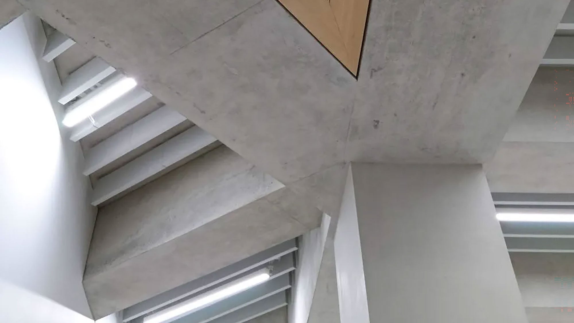 Architectural concrete columns and geometric ceiling slabs inside the Calgary Central Library, showcasing a smooth, light gray finish and integrated linear lighting.