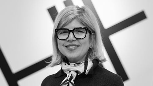 A black-and-white headshot of a woman in an ascot and glasses