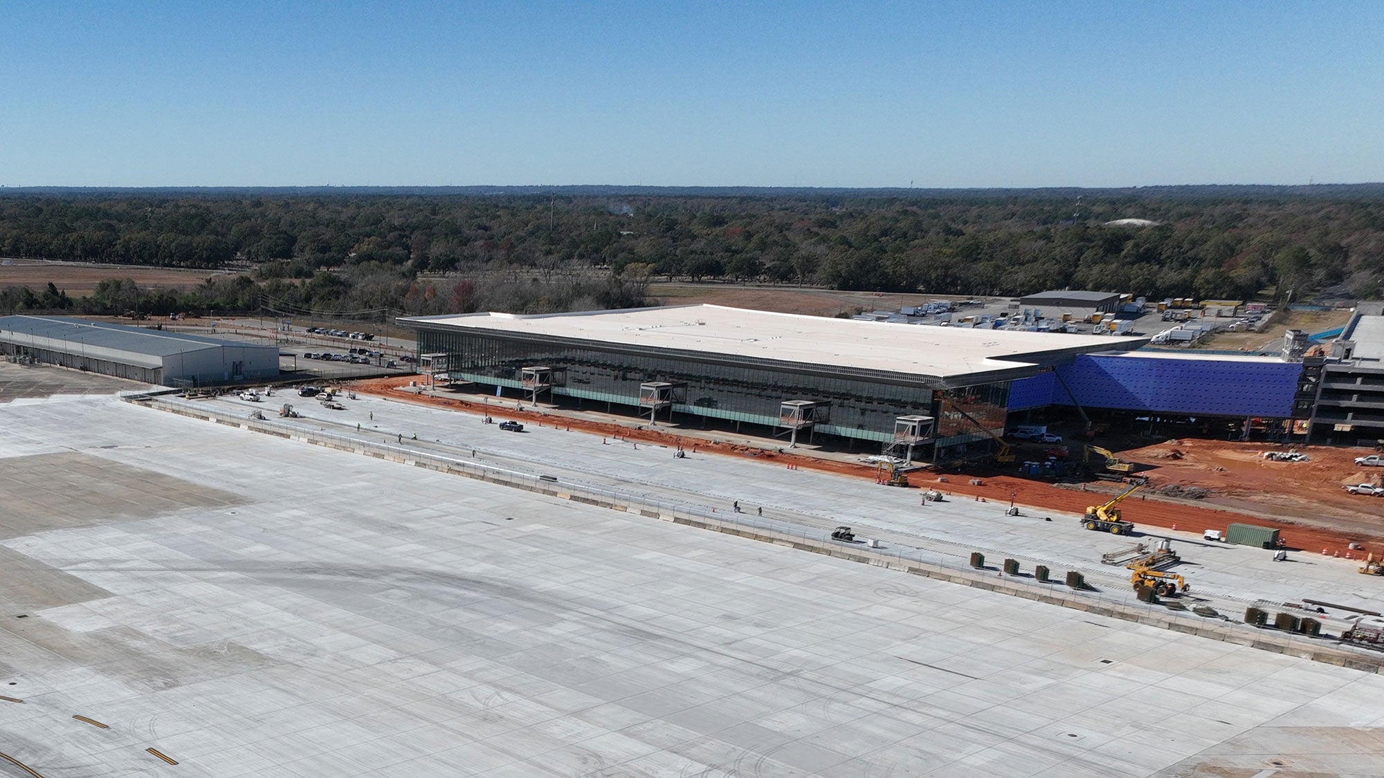 Wide-angle view of Movile's International Airport's terminal under construction, with a glass façade reflecting sunlight. Empty, expansive tarmac in the foreground.