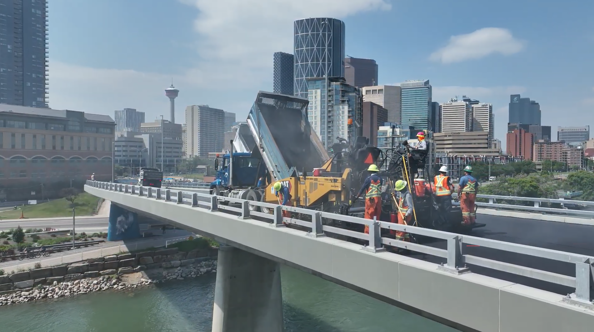 Construction workers lay paving on a bridge over a river