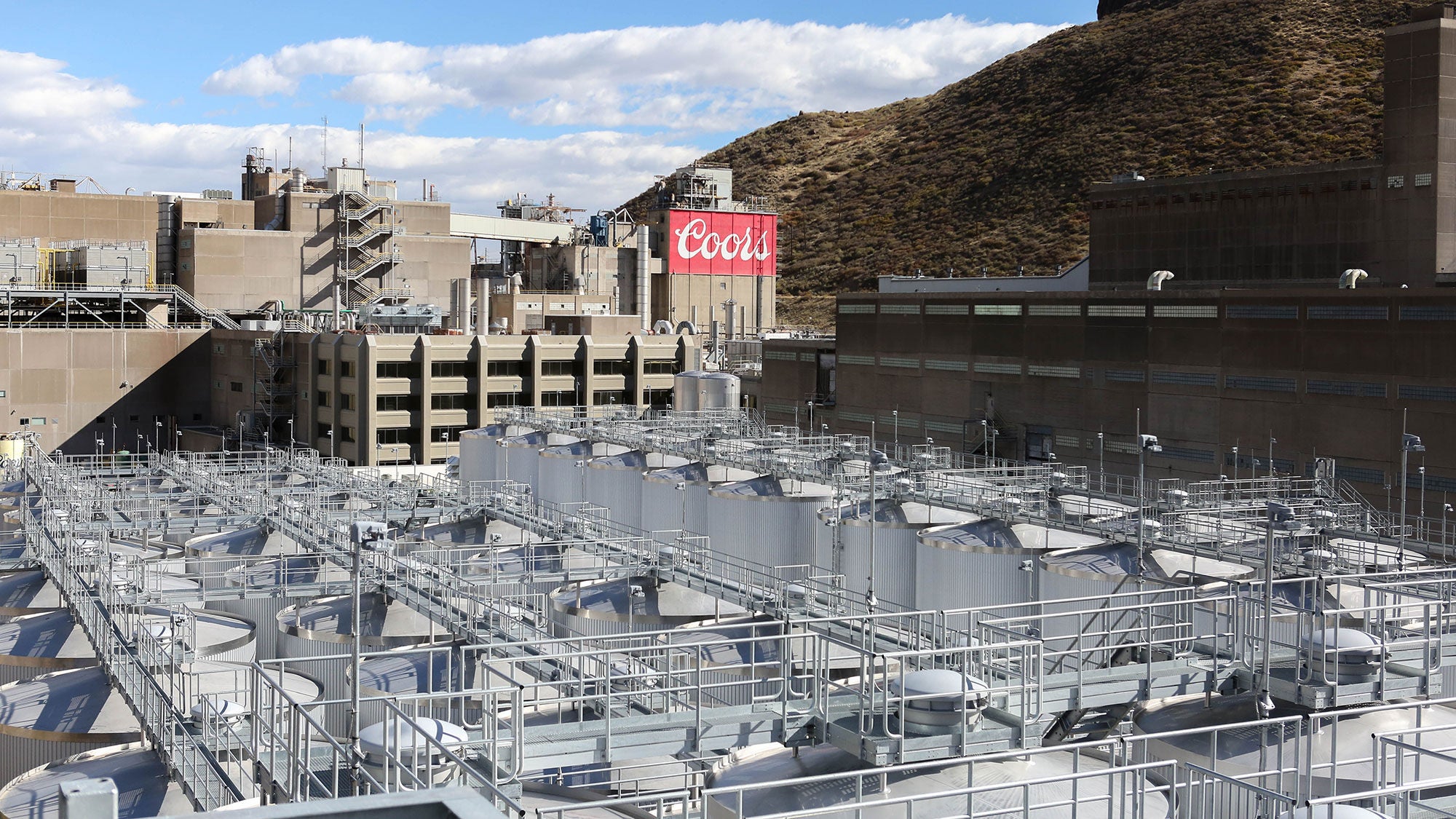 A complex matrix of beer tanks surrounded by a larger stone building with mountains behind it.