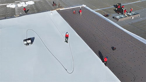 An aerial view of two workers installing a large white roof