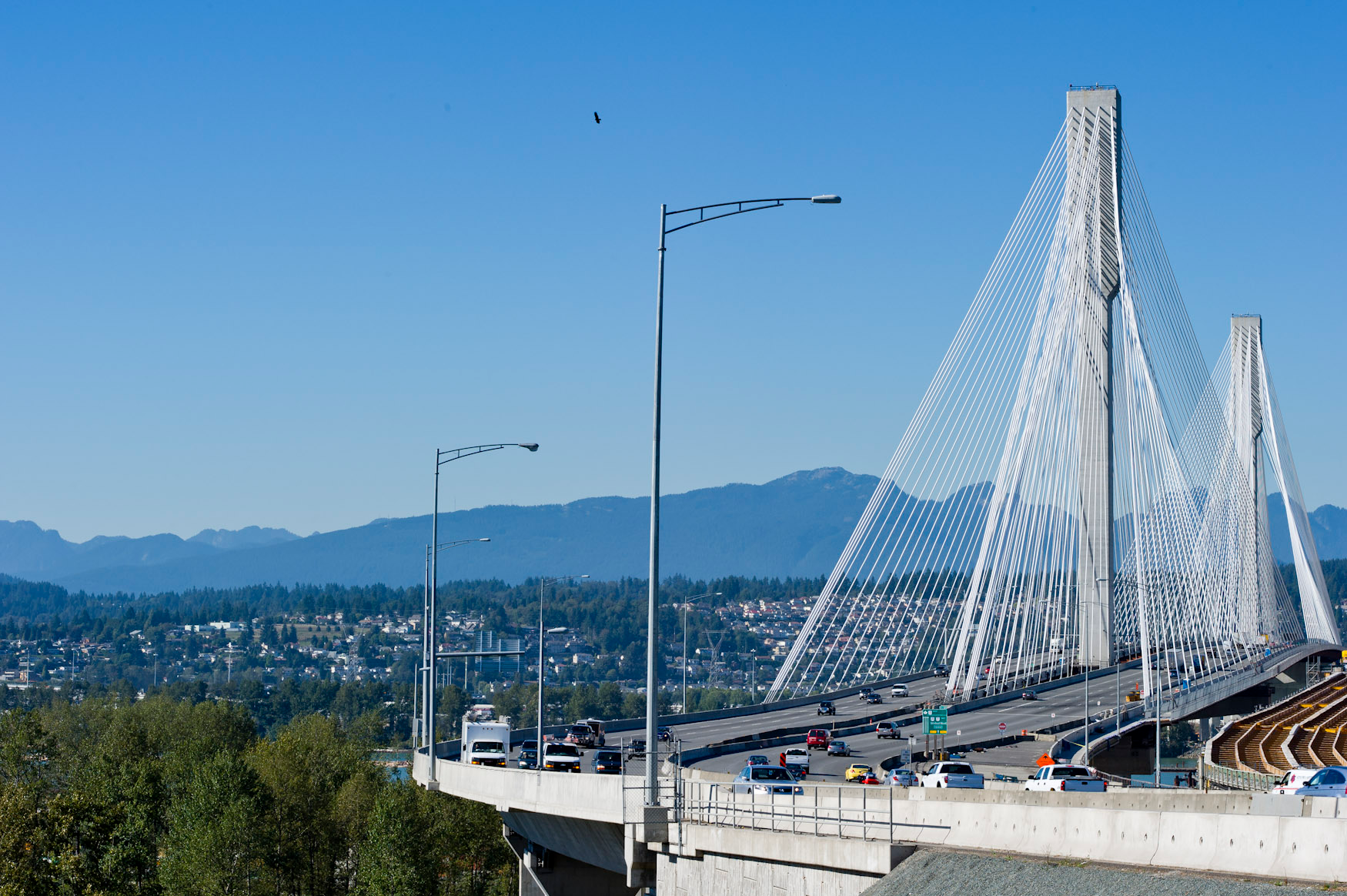 A large bridge with a central tower extending across an unseen river towards the mountains in the distance.