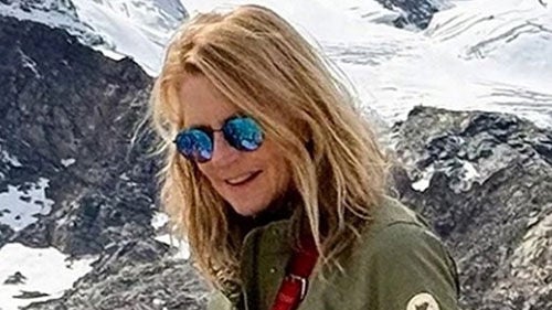 Nicole Sherman wearing sunglasses and a green utility jacket against a snowy mountain backdrop.