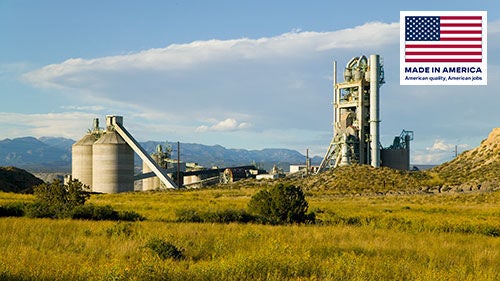 Silos and stacks of a cement plant set amongst the mountains and a clear blue sky