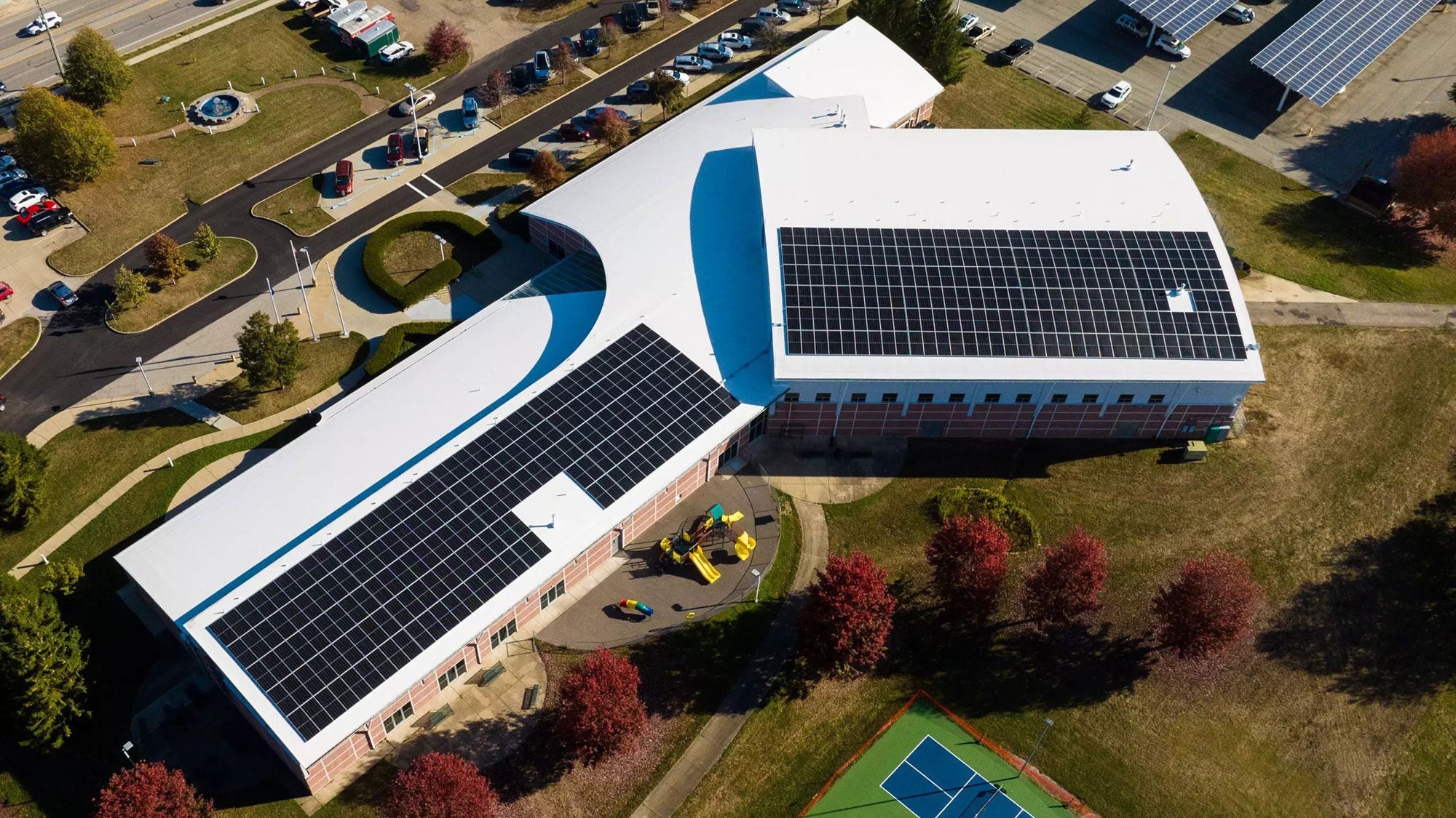 The back portion of a large, three armed building with a white roof and solar panels seen from above.