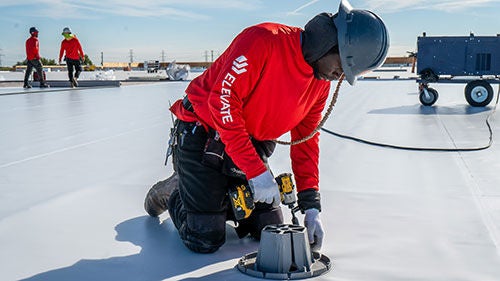A man in a red shirt using a drill to fasten a roofing system to a white roof