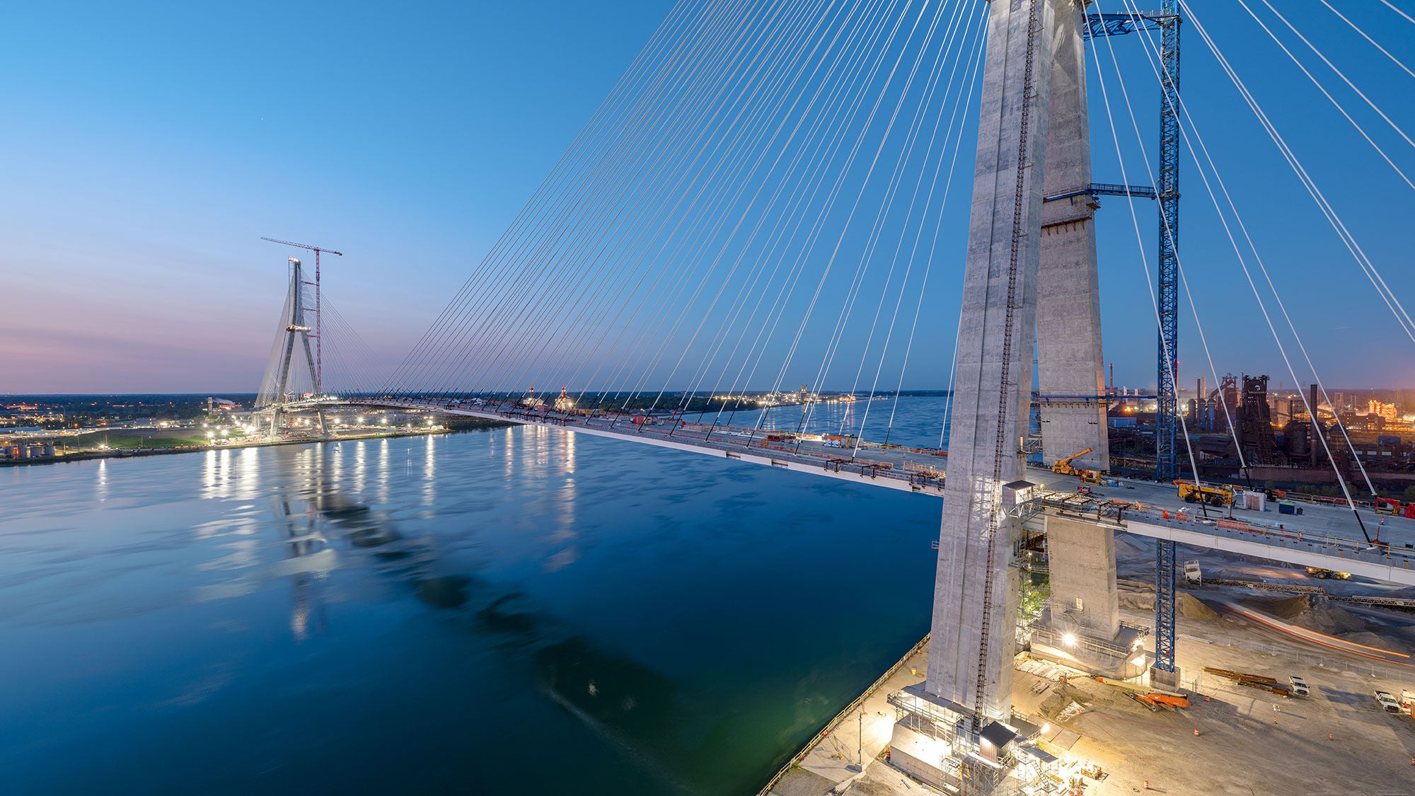 a large suspension bridge crosses a wide river at dusk