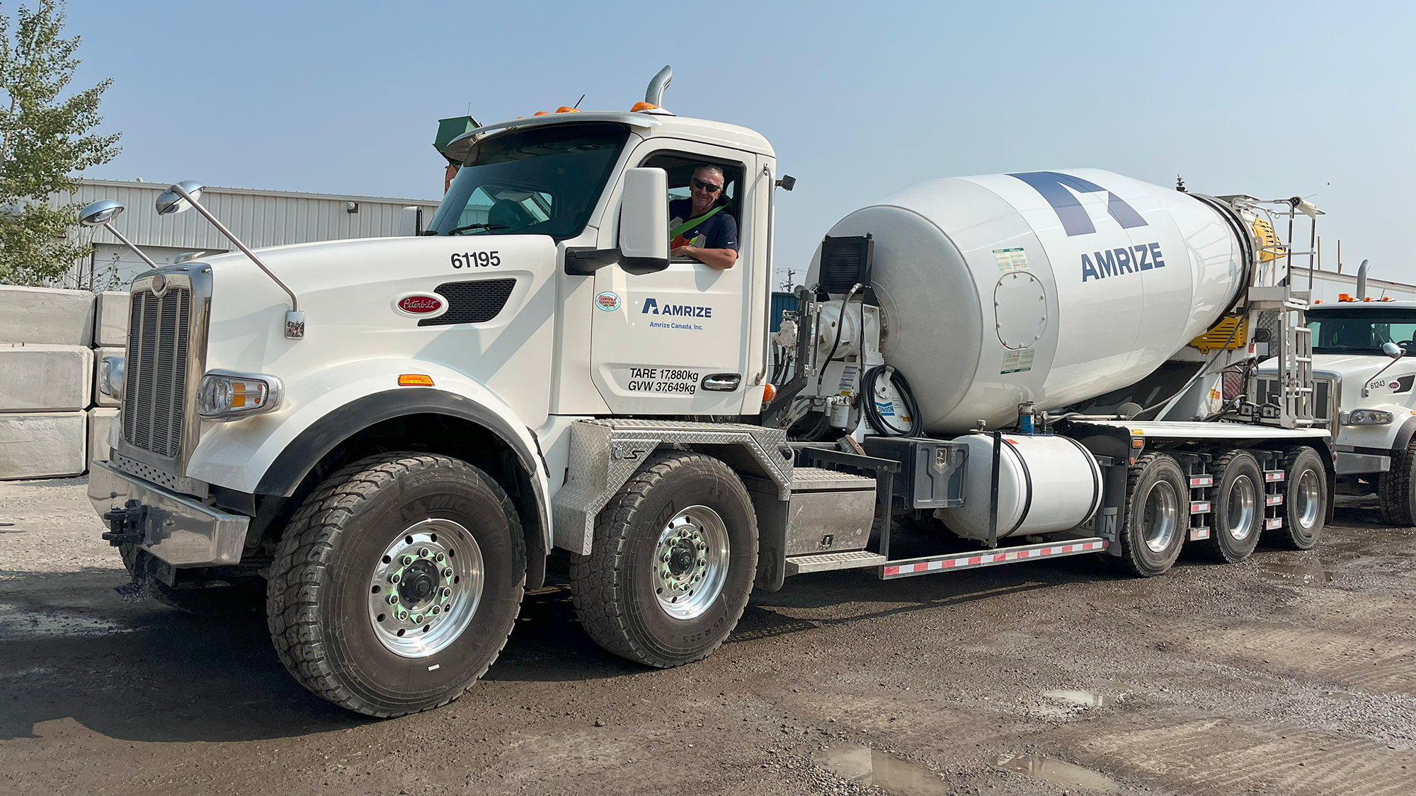A driver in the cab of his ready-mix truck leaning out of the window to look at the camera.