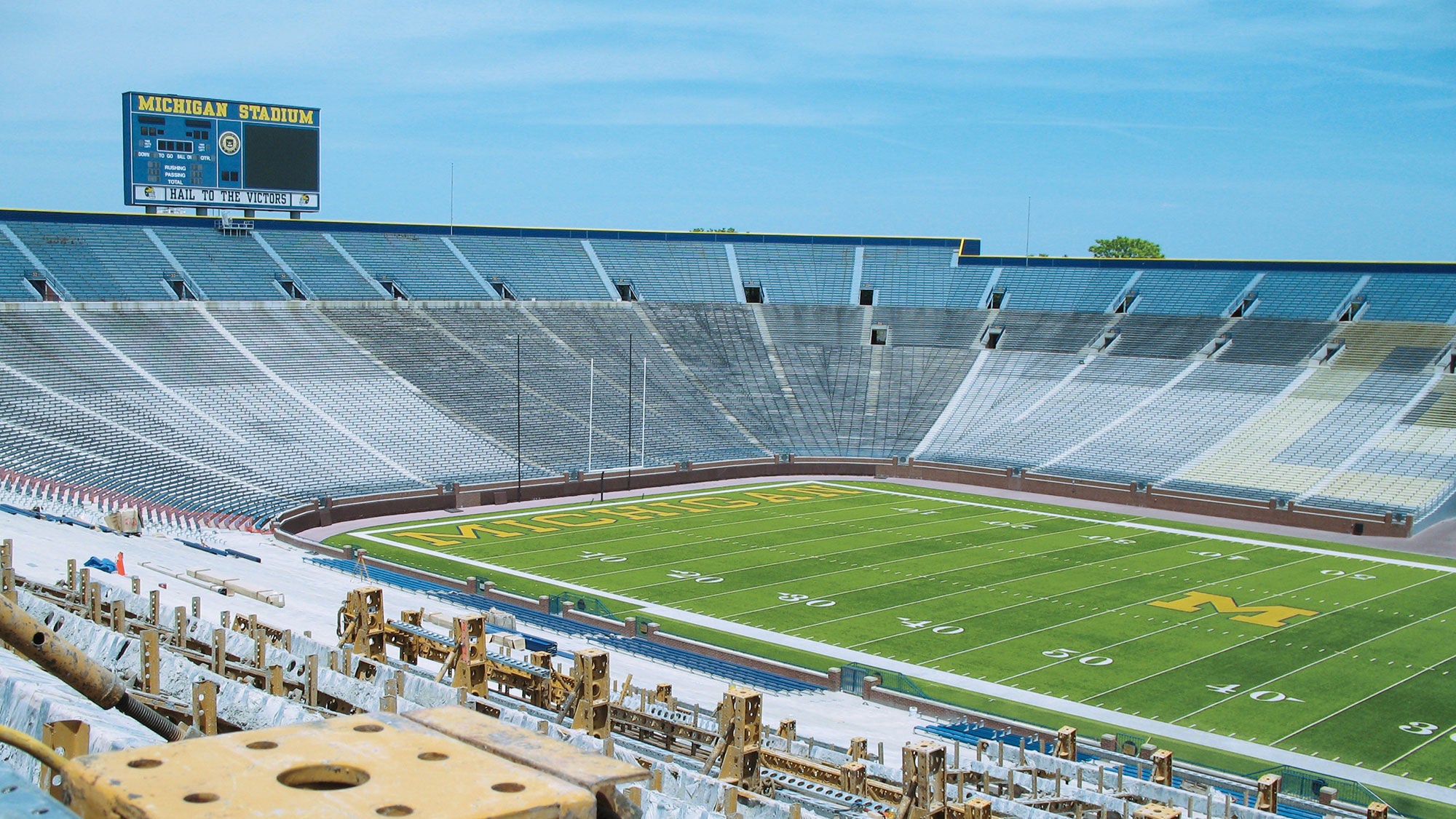 Looking down at Michigan Stadium's football field and large scoreboard from an upper deck section undergoing renovation or construction.
