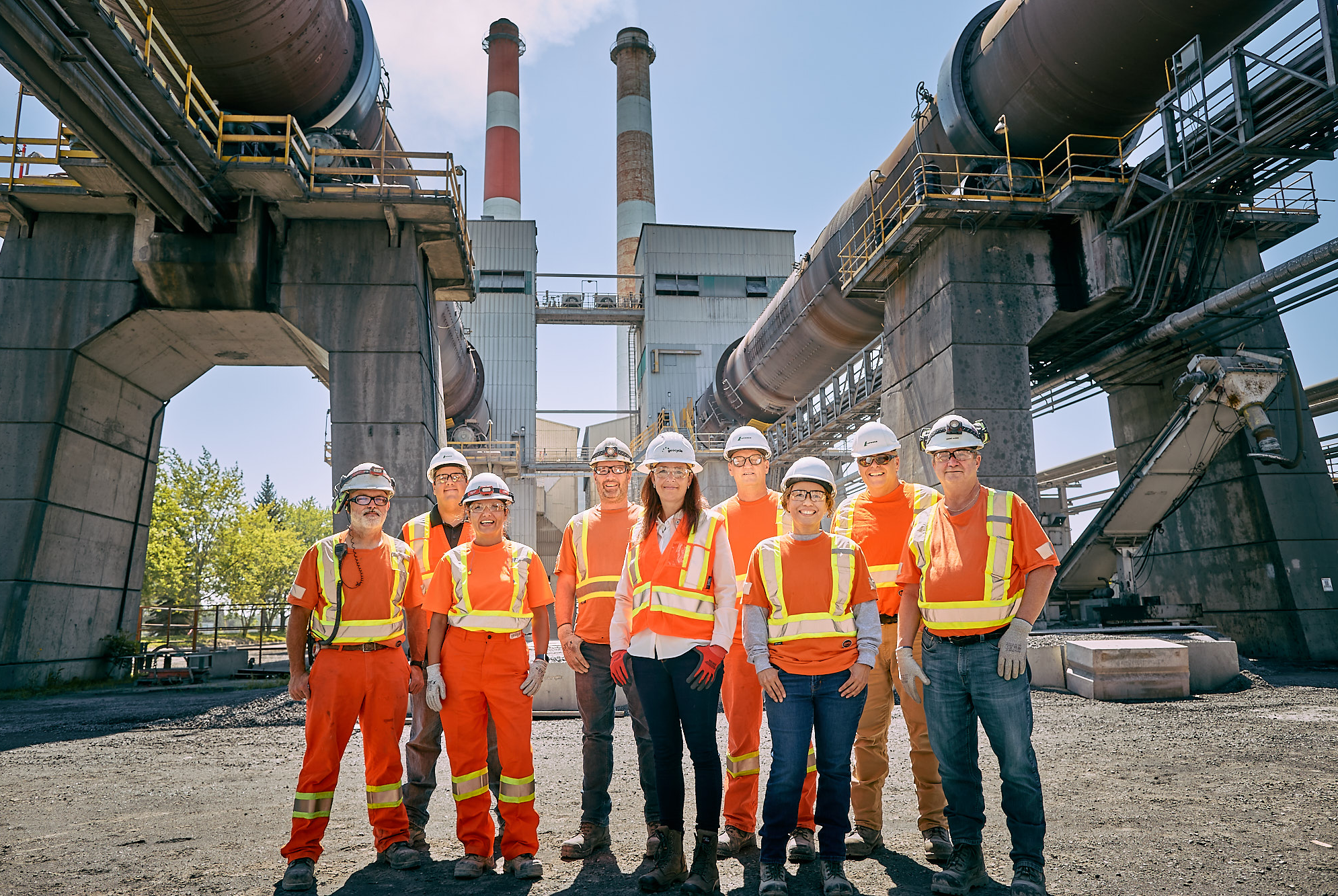 A group of men and women wearing protective gear standing against the backdrop of a cement plant