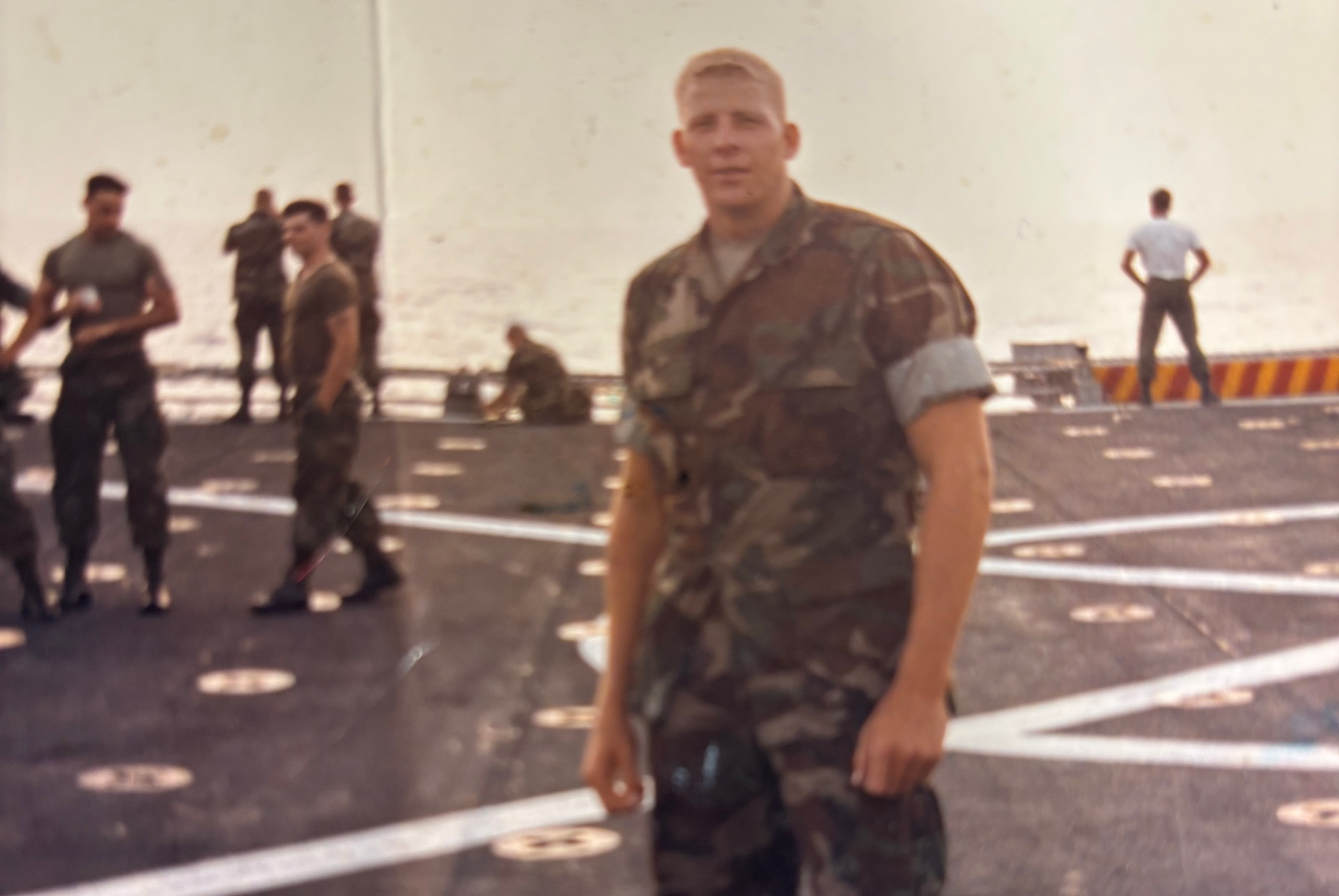 A man in a U.S. Marine Corps uniform with other Marines in the background.