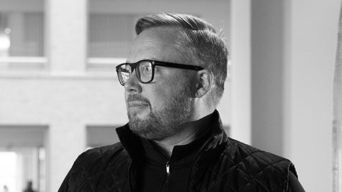 A black-and-white headshot of a man with short hair and glasses