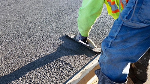 A man bends over fresh concrete to smooth it with a tool